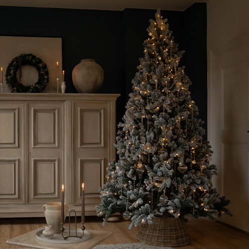 Künstlicher, schneebedeckter Weihnachtsbaum mit warmen Lichtern und Dekoration in einem gemütlichen Raum