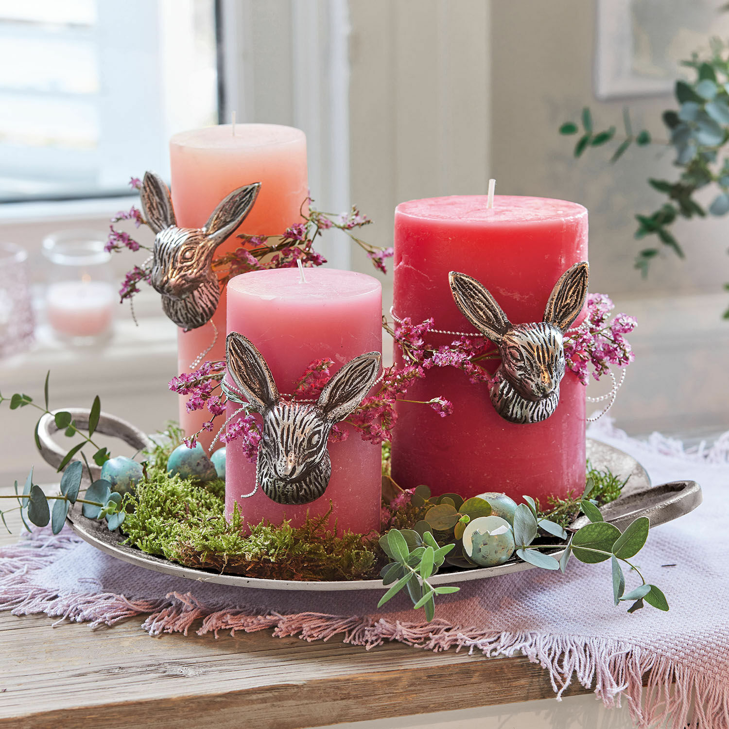 Kerze 3er Set Pretin Drei rosa Kerzen mit Hasenkopf-Dekor und grünem Moos auf einem Metalltablett arrangiert