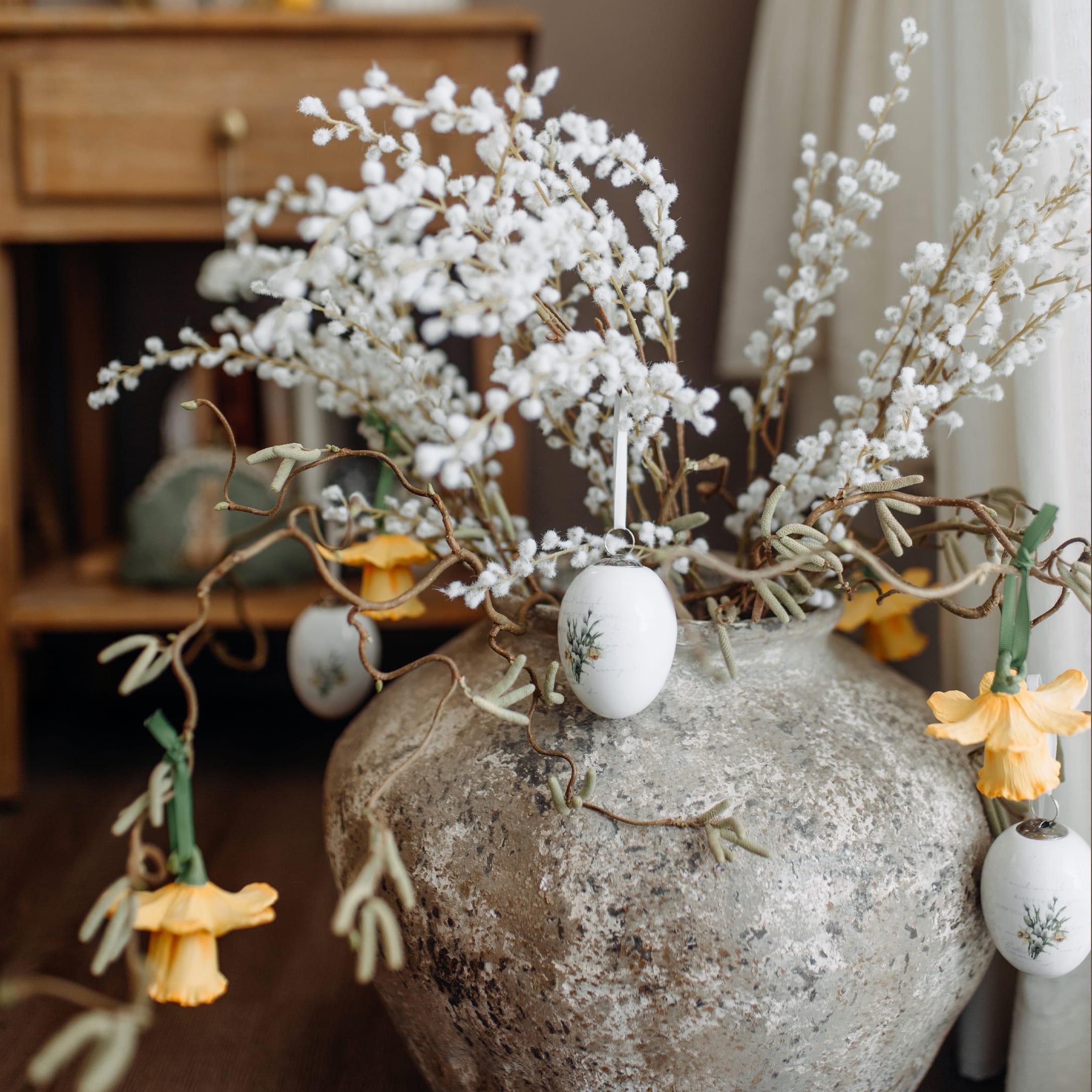 Grosse graue Keramikvase mit weissen Zweigen und gelben Blumen als Frühlingsdekoration im Raum
