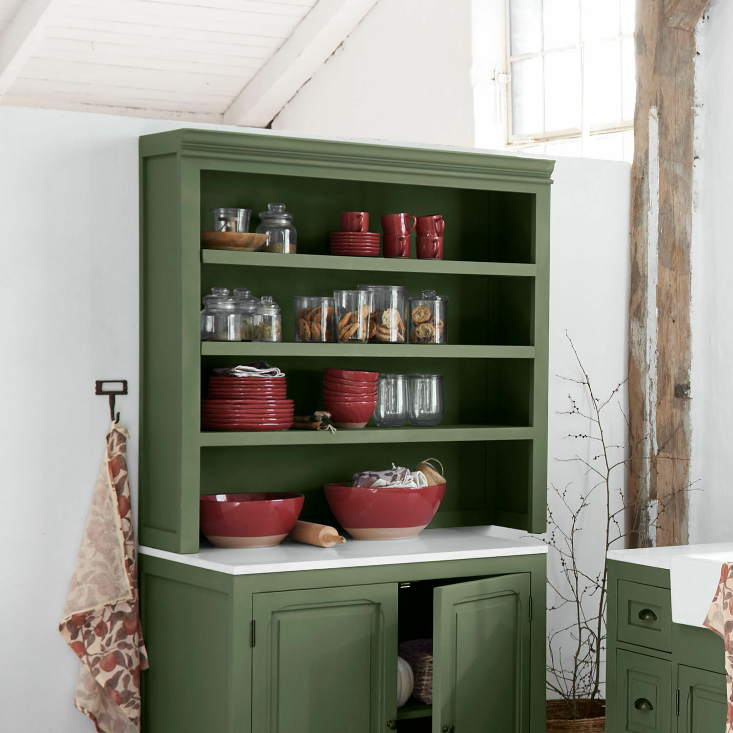 Grüner Holz-Küchenschrank mit roten Keramikschalen und Glasbehältern mit Keksen in rustikaler Küche