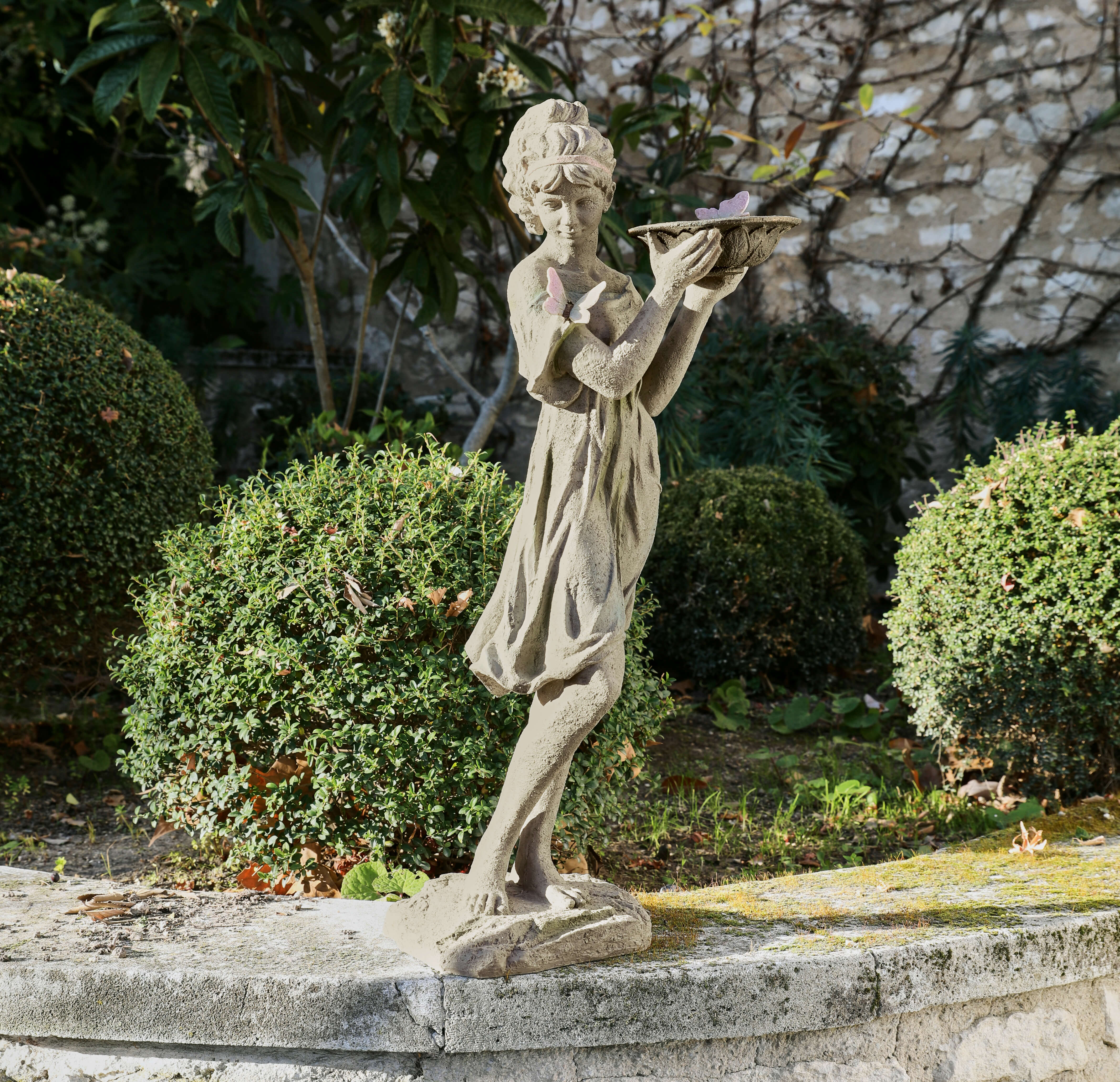 Beton-Gartenfigur eines Mädchens mit Schmetterlingen, dekorativ im grünen Garten platziert