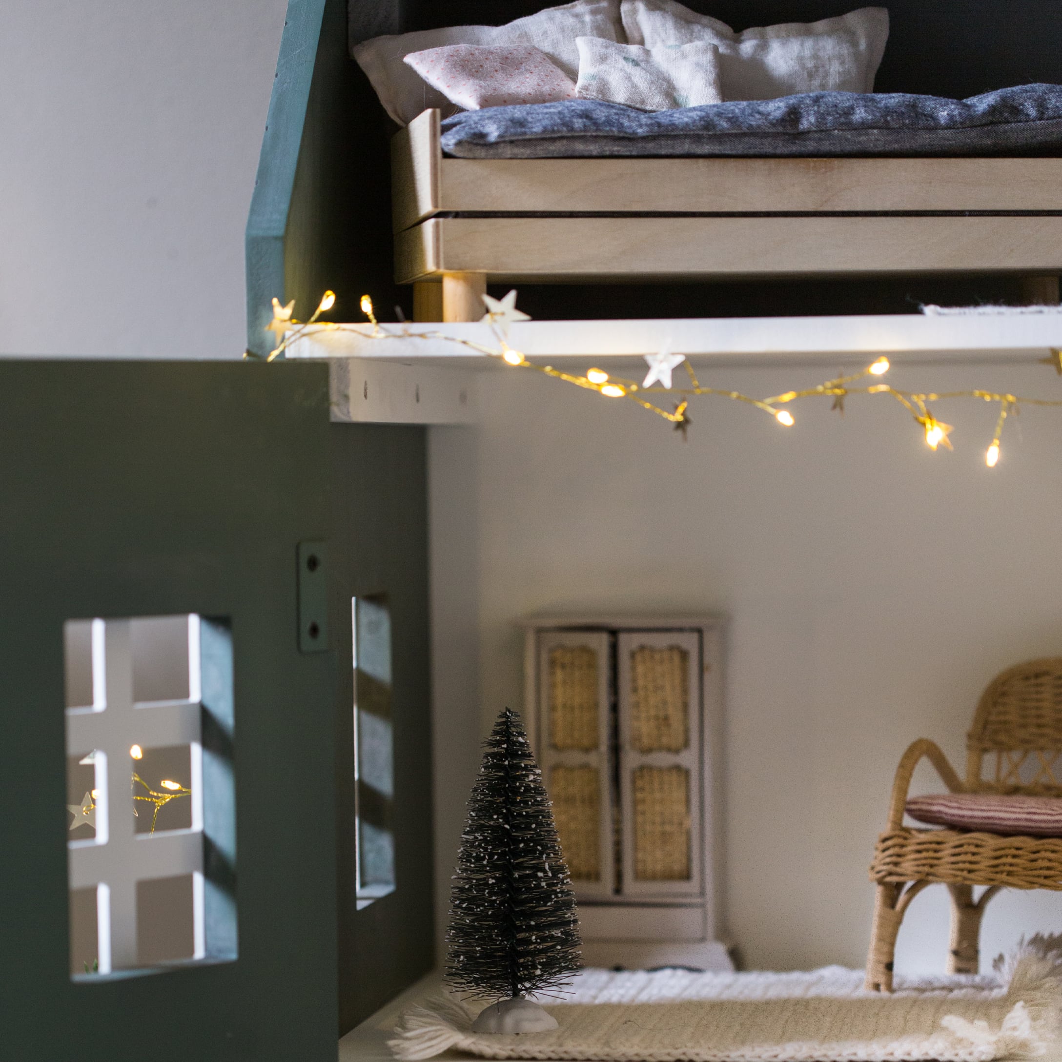Kleiner schwarzer Deko-Tannenbaum aus Fasern auf weissem Teppich in gemütlichem Kinderzimmer mit Lichterkette