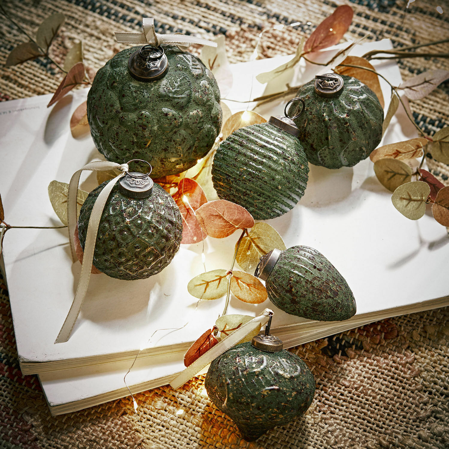 Weihnachtsschmuck 6er Set Moriches Set aus grünen, strukturierten Weihnachtskugeln mit Bändern auf weissem Buch auf Naturteppich