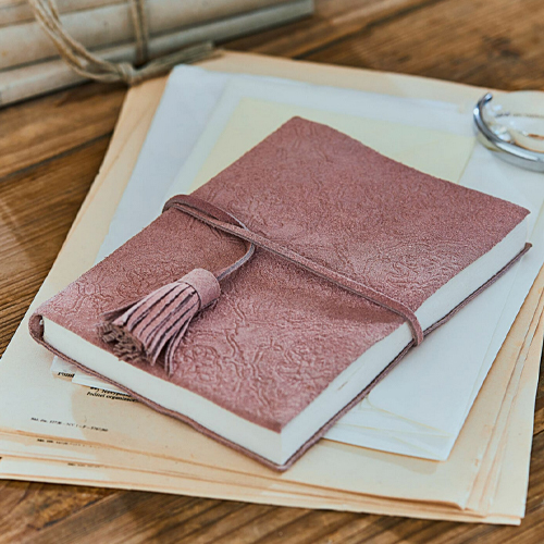 Rosa Notizbuch aus weichem, geprägtem Leder mit Quaste auf Holztisch mit Papieren