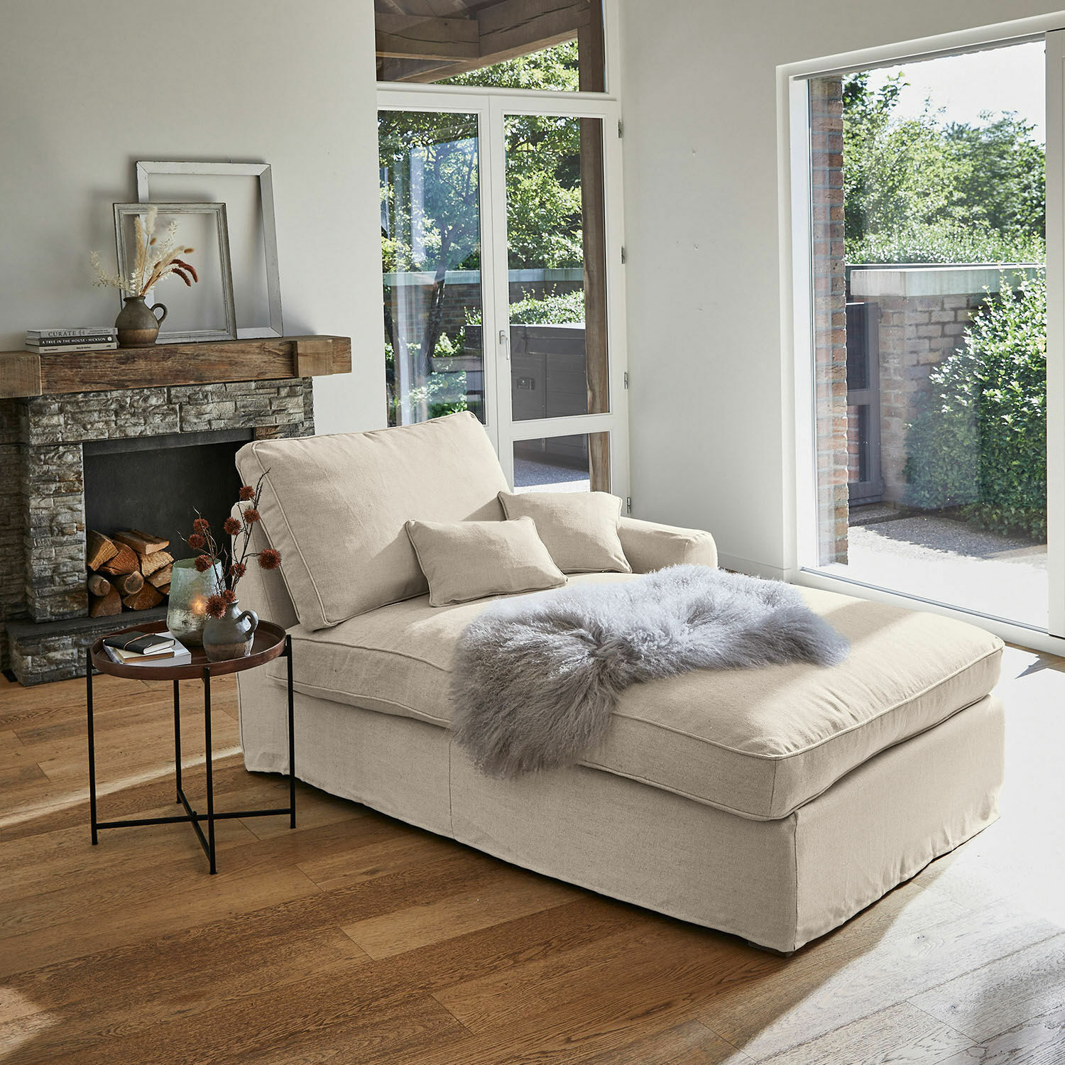 Beige Stoff-Chaiselongue mit Kissen und grauem Fellüberwurf in hellem Wohnzimmer mit Cheminée