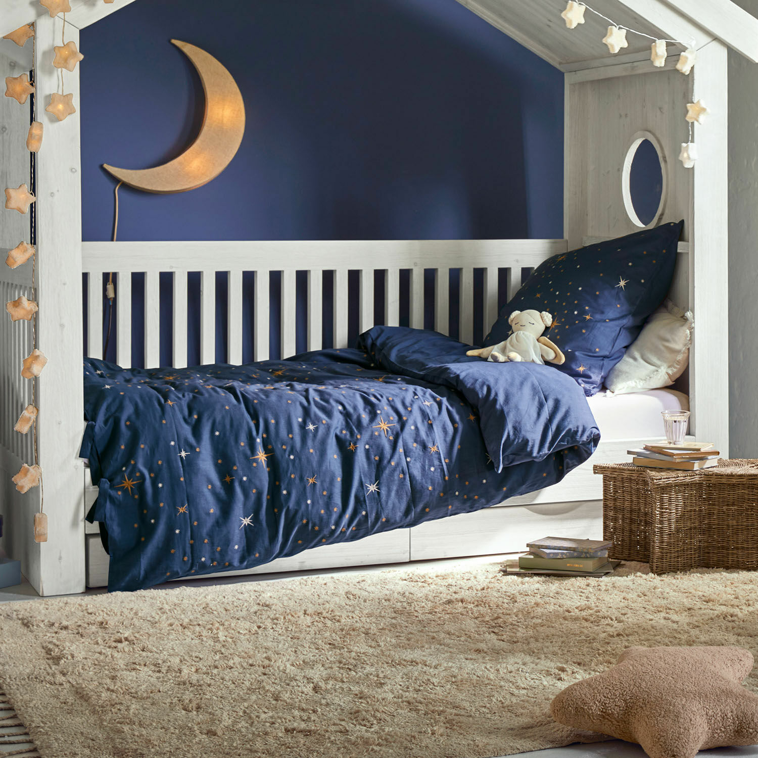 Bettwäsche Starwhisper Weisses Kinderbett aus Holz mit dunkelblauer Sternenbettwäsche und Mondlampe im gemütlichen Kinderzimmer