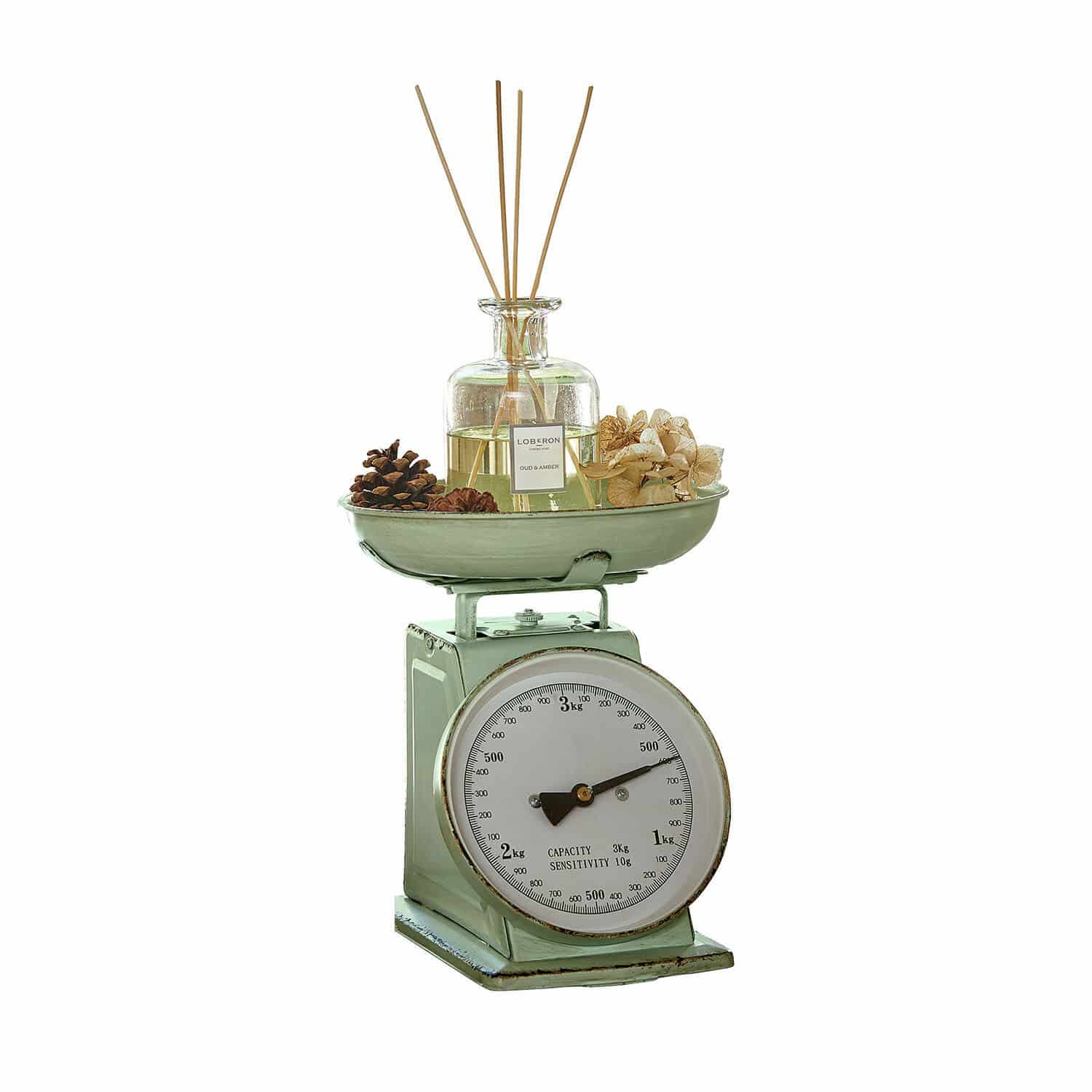 Grüne Metall-Küchenwaage mit weissem Zifferblatt und dekorativem Duftflakon mit Stäbchen