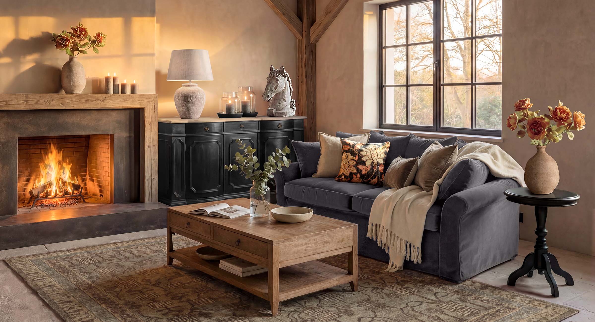Gemütliches Wohnzimmer mit Cheminée, Holztisch, grauem Sofa und Dekorationen aus Blumen und Kerzen