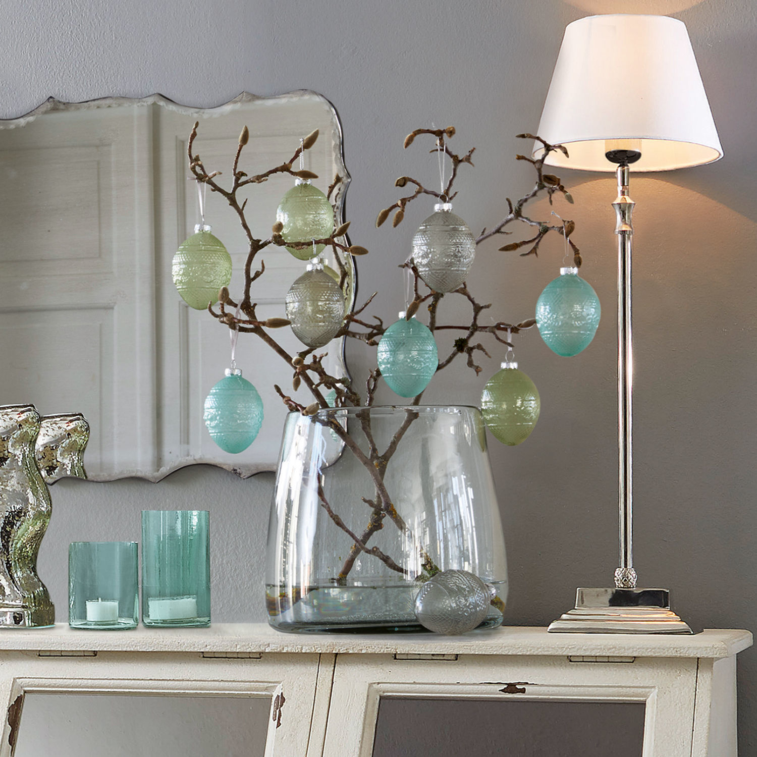 Vase Inga Dekorative Glaseier in Pastellfarben an Zweigen in klarer Glasvase auf weissem Sideboard