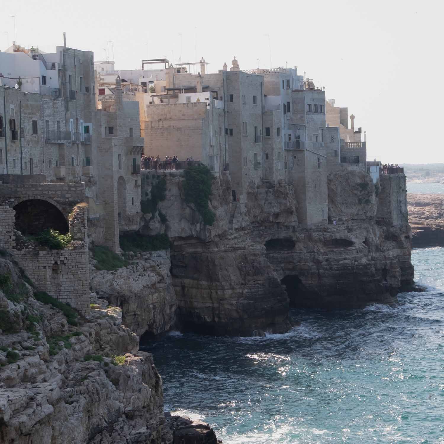 Alte steinerne Gebäude auf Klippe über dem Meer mit Touristen und Wellen am Küstenabschnitt