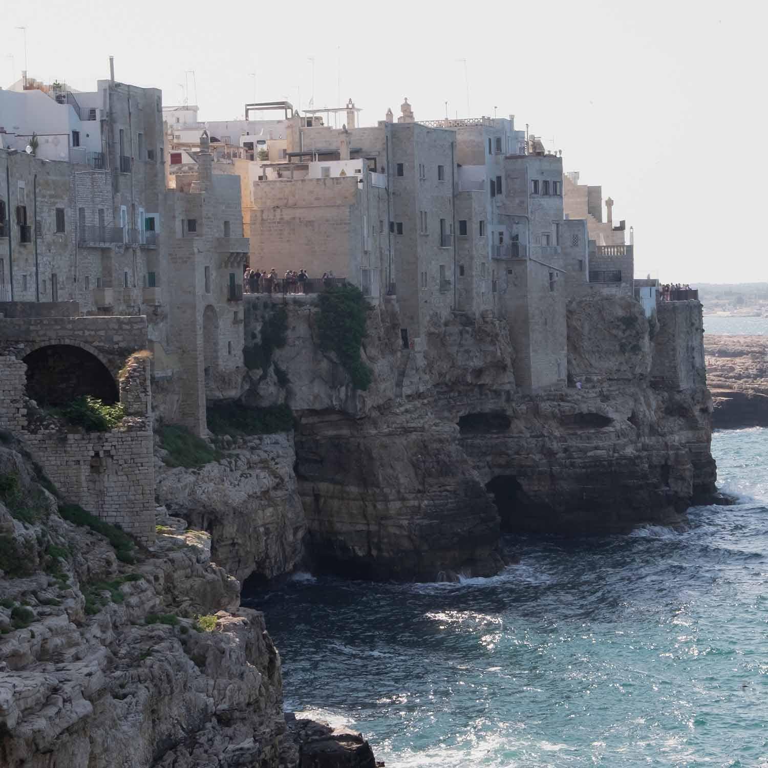 Alte steinerne Gebäude auf Klippe über dem Meer mit Touristen und Wellen am Küstenabschnitt