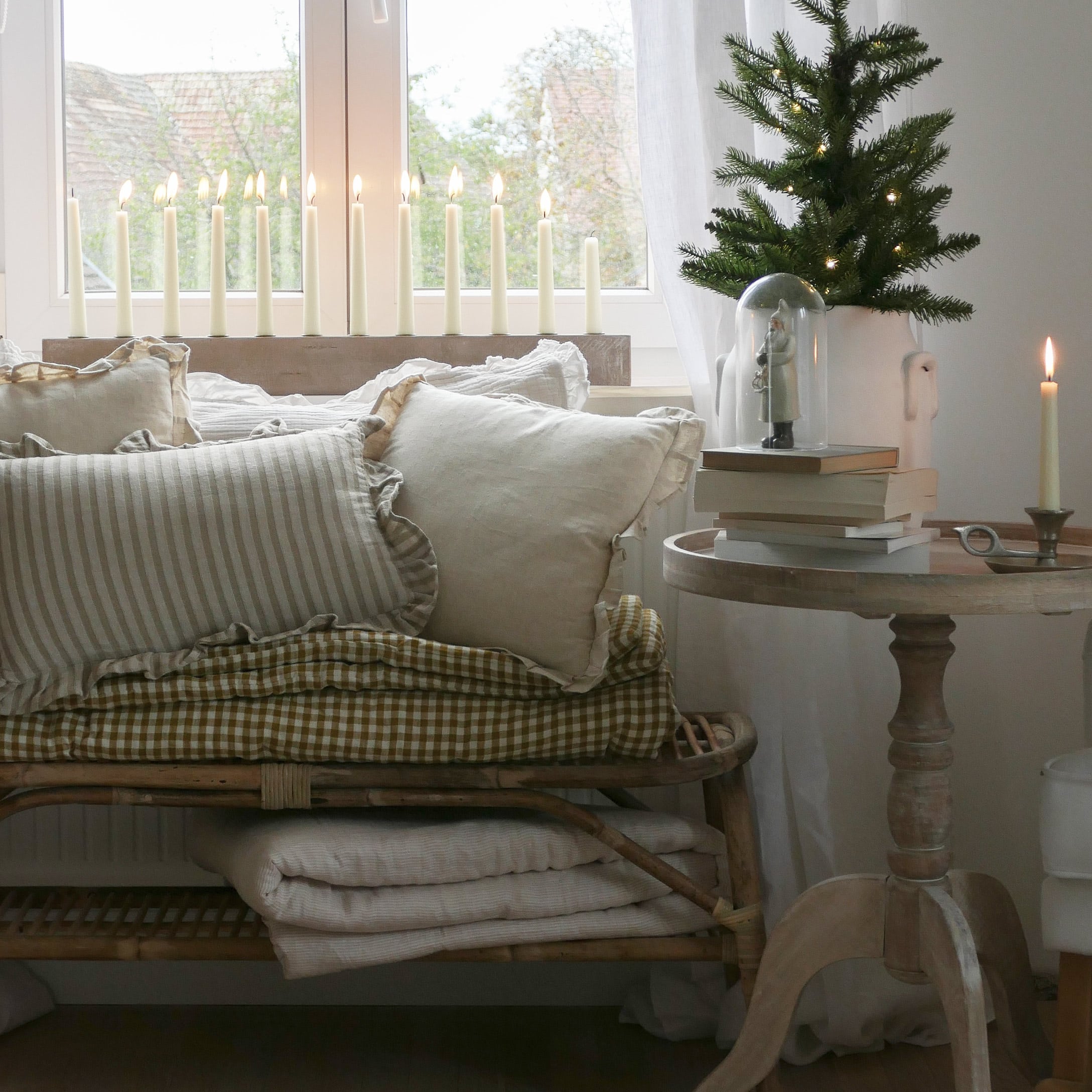 Gemütliche Ecke mit beigen Kissen und Holztisch mit Dekorationen und brennenden Kerzen