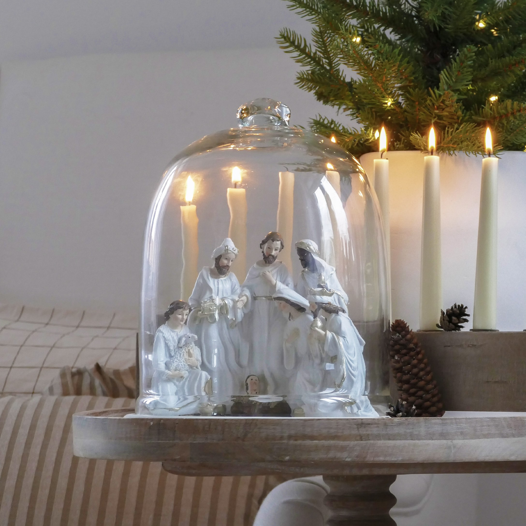 Weisse Keramikkrippe unter Glashaube mit brennenden Kerzen und weihnachtlicher Dekoration