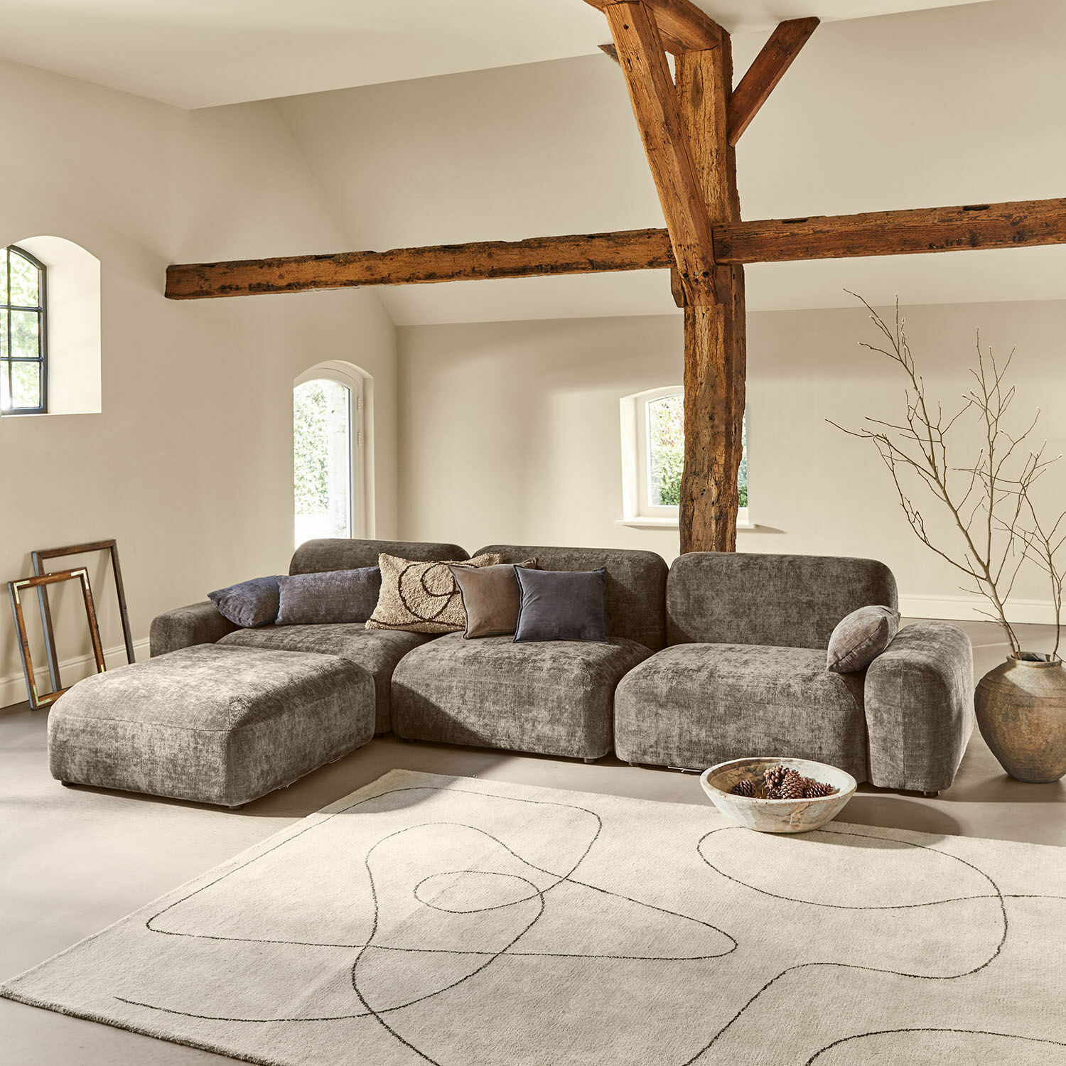 Sofa Marnivelle Graues, modular aufgebautes Sofa aus Stoff in modernem Wohnzimmer mit Holzbalken und hellem Teppich