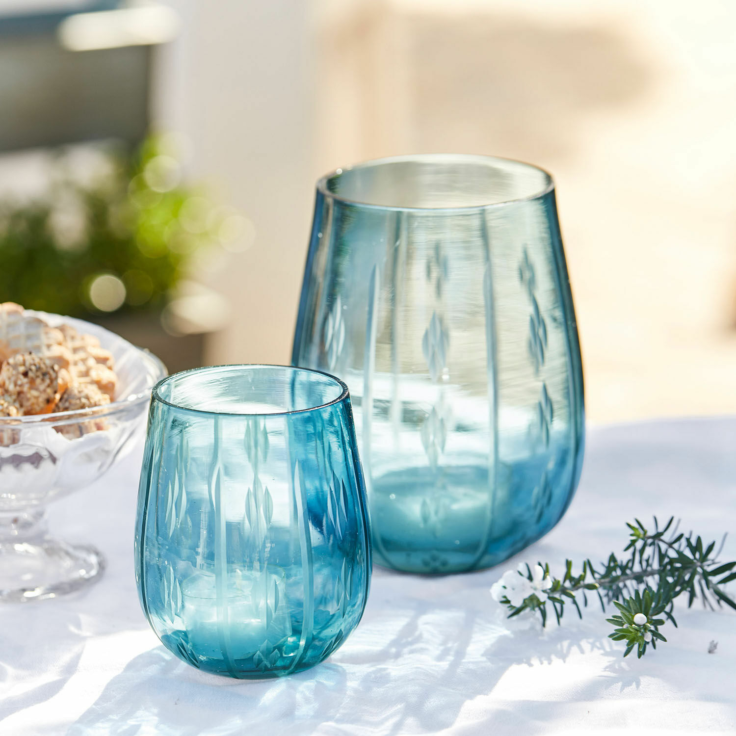 Zwei blaue Glaswindlichter mit graviertem Muster auf weiss-lichem Hintergrund, Tischdekoration