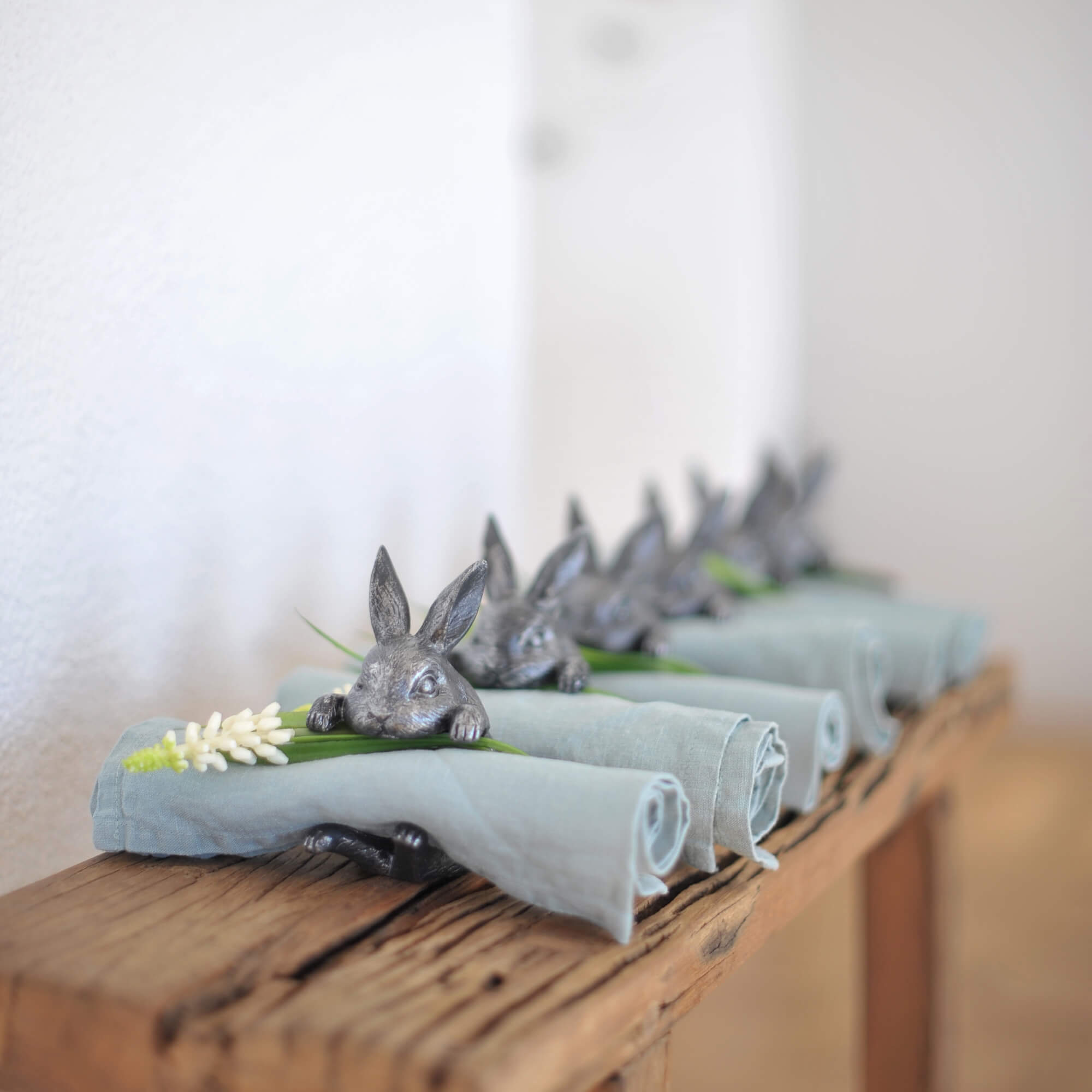 Metallene silberne Serviettenringe mit Hasenmotiv und blauen Leinenservietten auf Holztisch