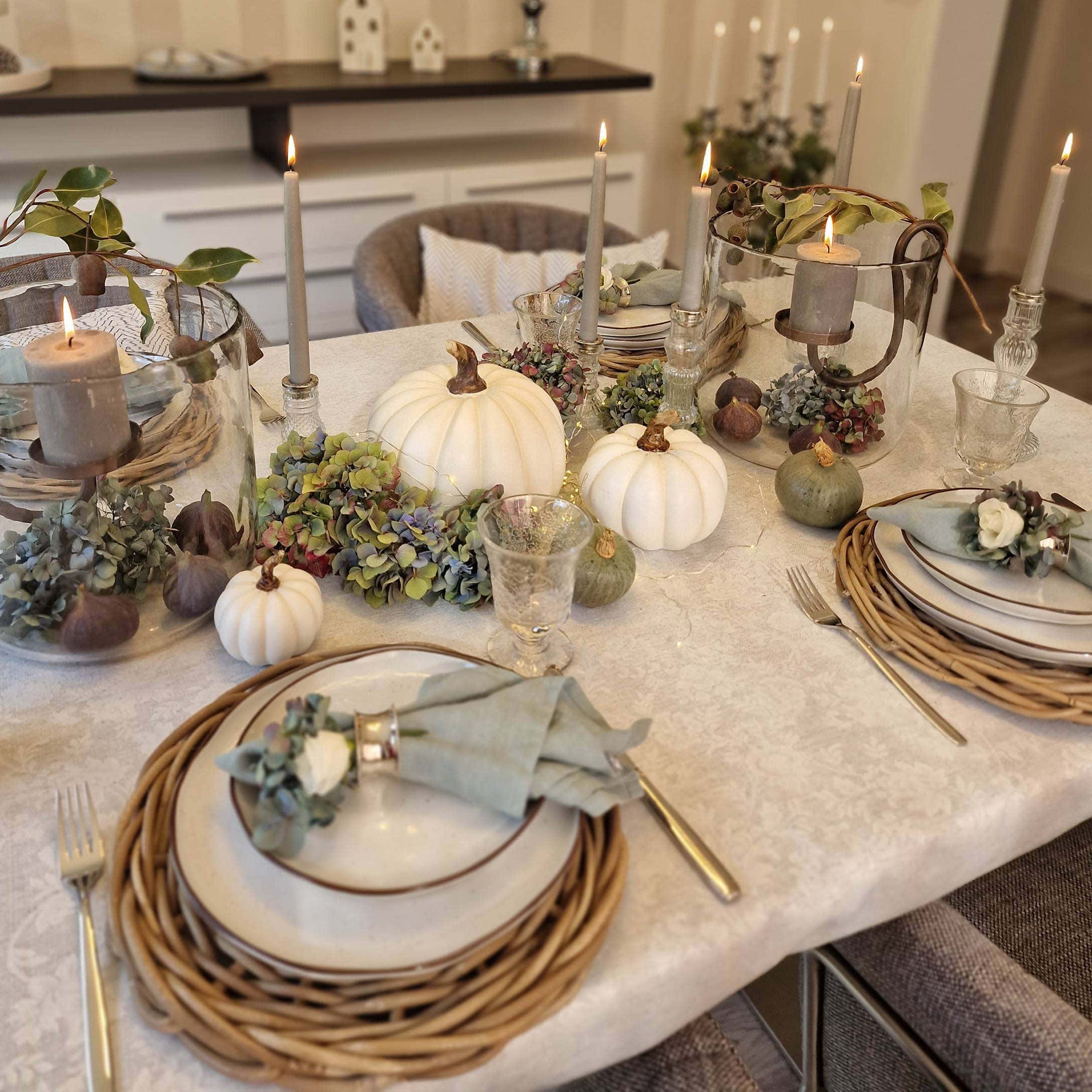 Elegante Herbsttischdekoration mit weissen Kürbissen, Kerzen und natürlichen Akzenten auf der Tischdecke