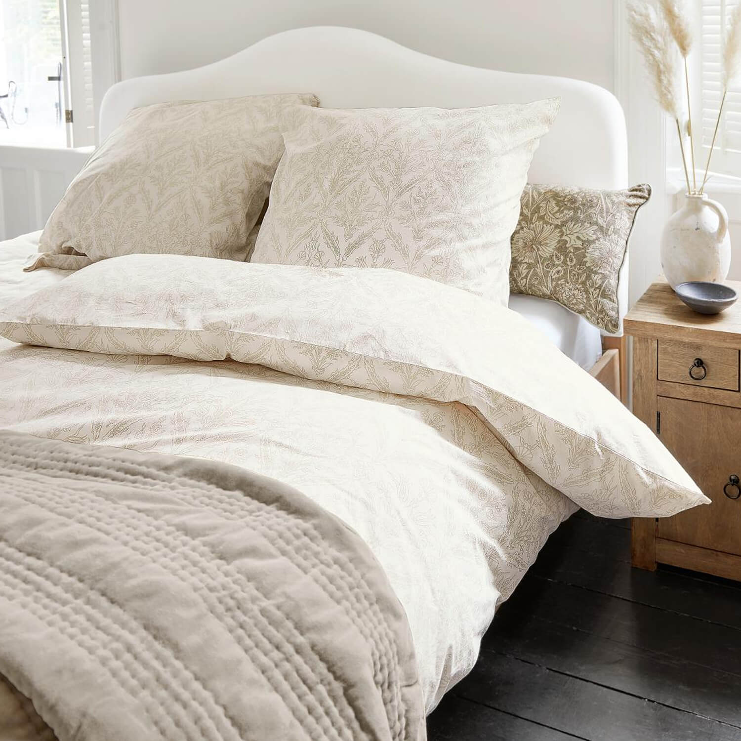 Baumwoll-Bettwäsche in hellen Farben mit feinem Pflanzenmuster und weicher Decke auf weissem Bett