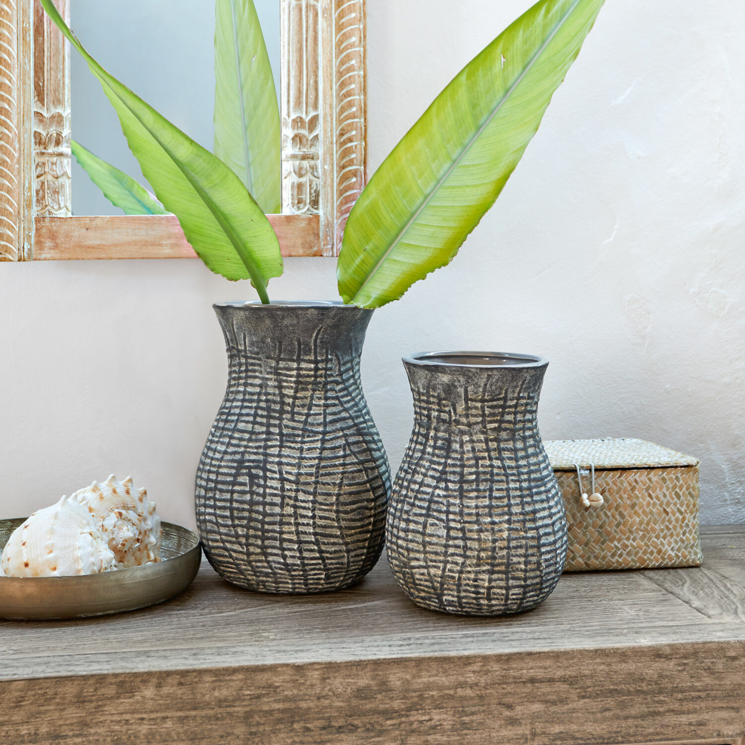 Vase 2er Set Fahrid Zwei graue Keramikvasen mit strukturiertem Muster auf einem Holztisch, dekoriert mit grünen Blättern