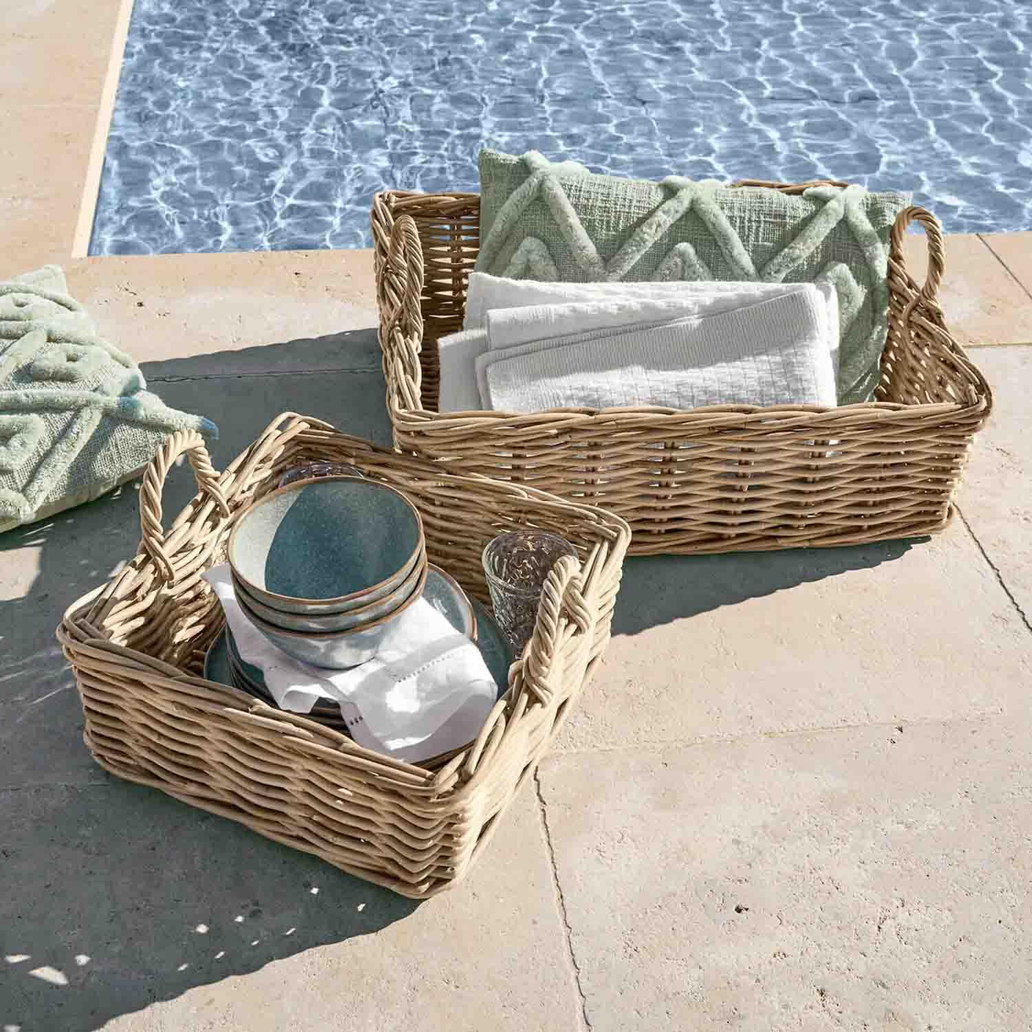 Zwei geflochtene Körbe mit Griffen, gefüllt mit grünen Kissen und weißen Handtüchern, neben dem Pool