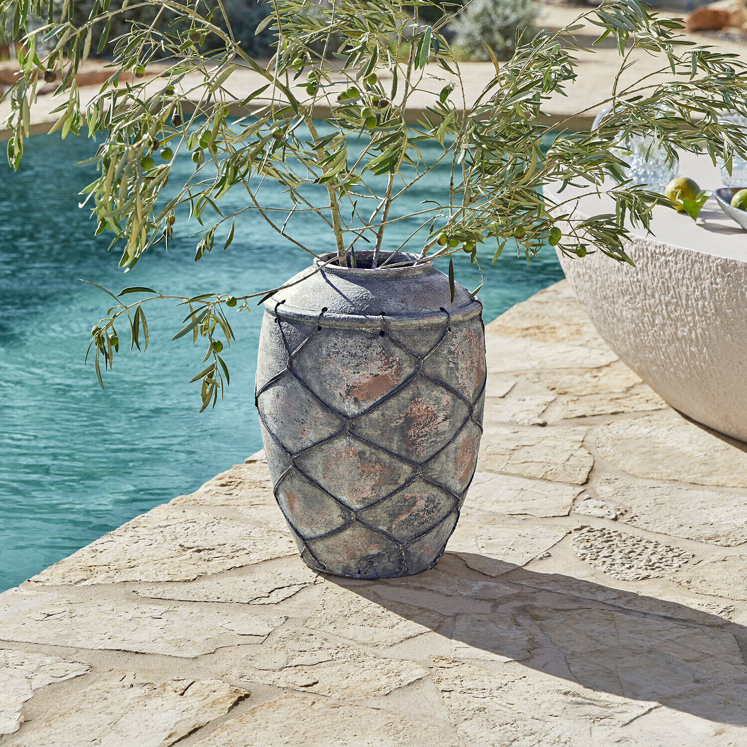 Vase Deloriva Große graue Keramikvase mit Netzdekor auf Stein-Terrasse neben Pool mit Olivenzweigen