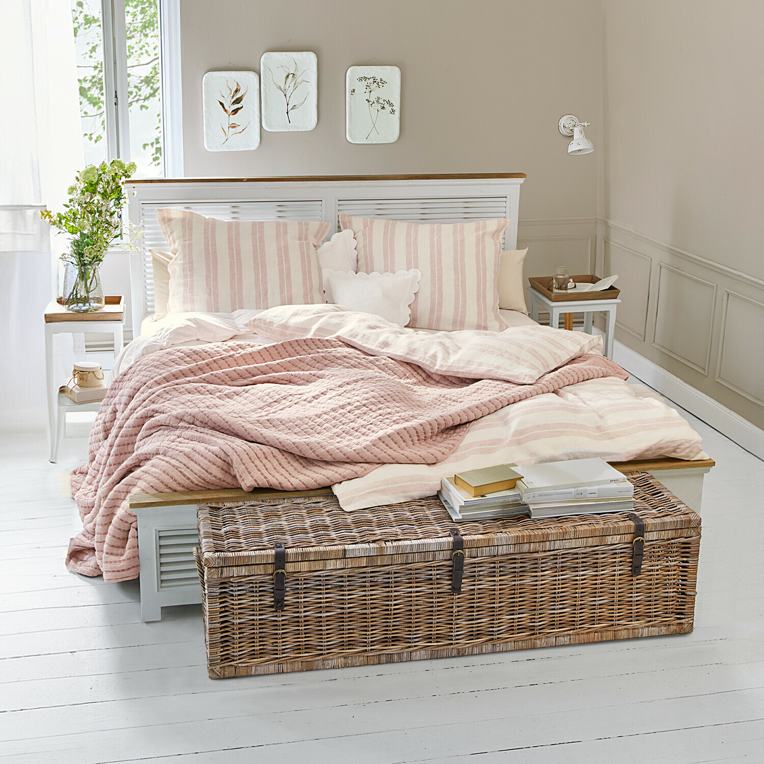 Gemütliches Schlafzimmer mit hellrosa gestreiftem Bett und Korbtruhe auf weissem Boden