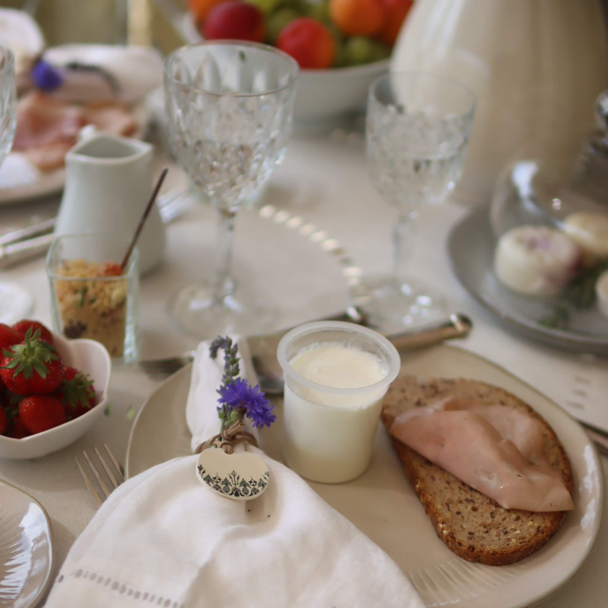 Frühstückstisch mit Vollkornbrot, Schinken und Joghurt auf dem Teller, Serviette mit Blumendekor