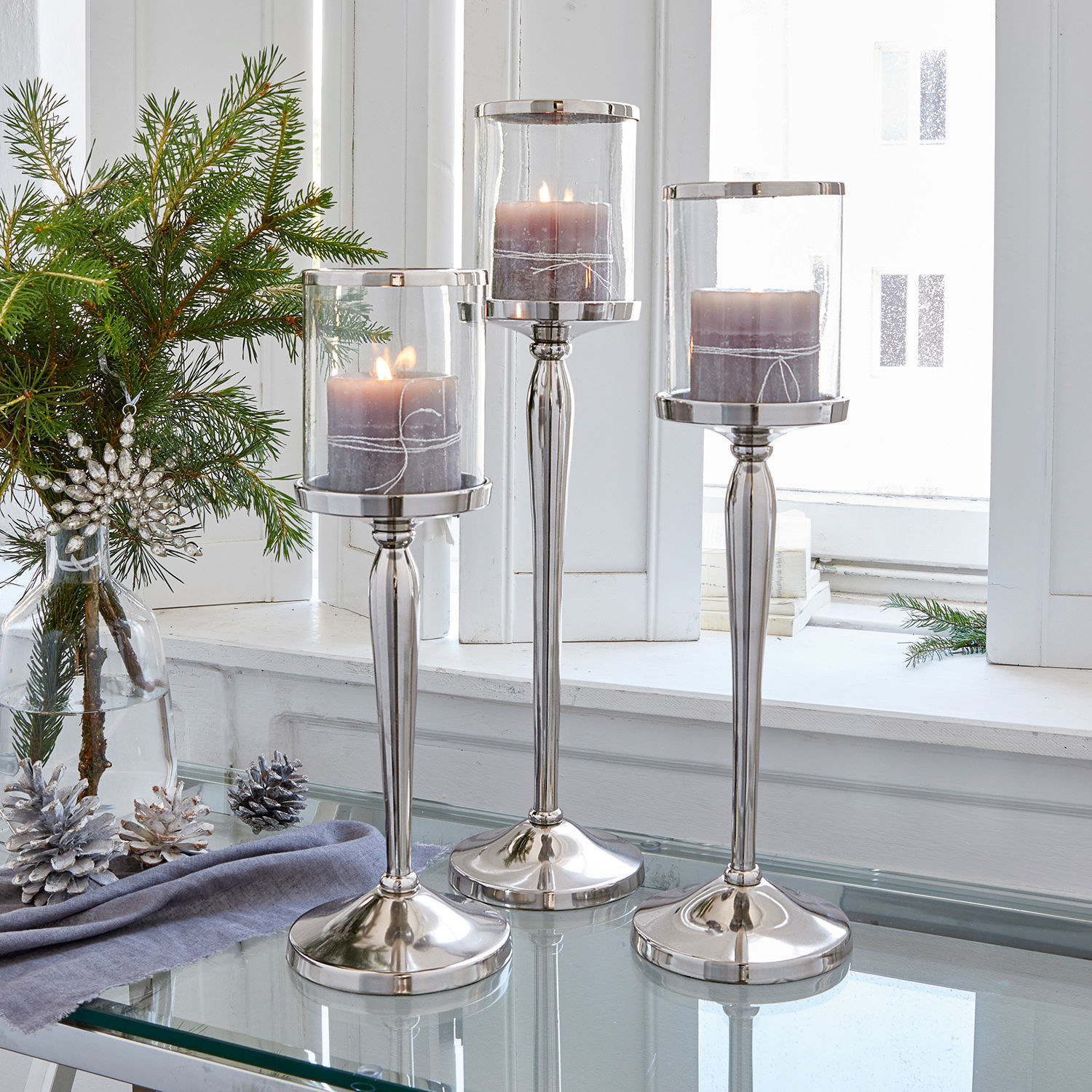 Kerzenständer 3er Set Serres Drei silberne Kerzenhalter aus Glas und Metall mit violetten Kerzen auf einem Glastisch