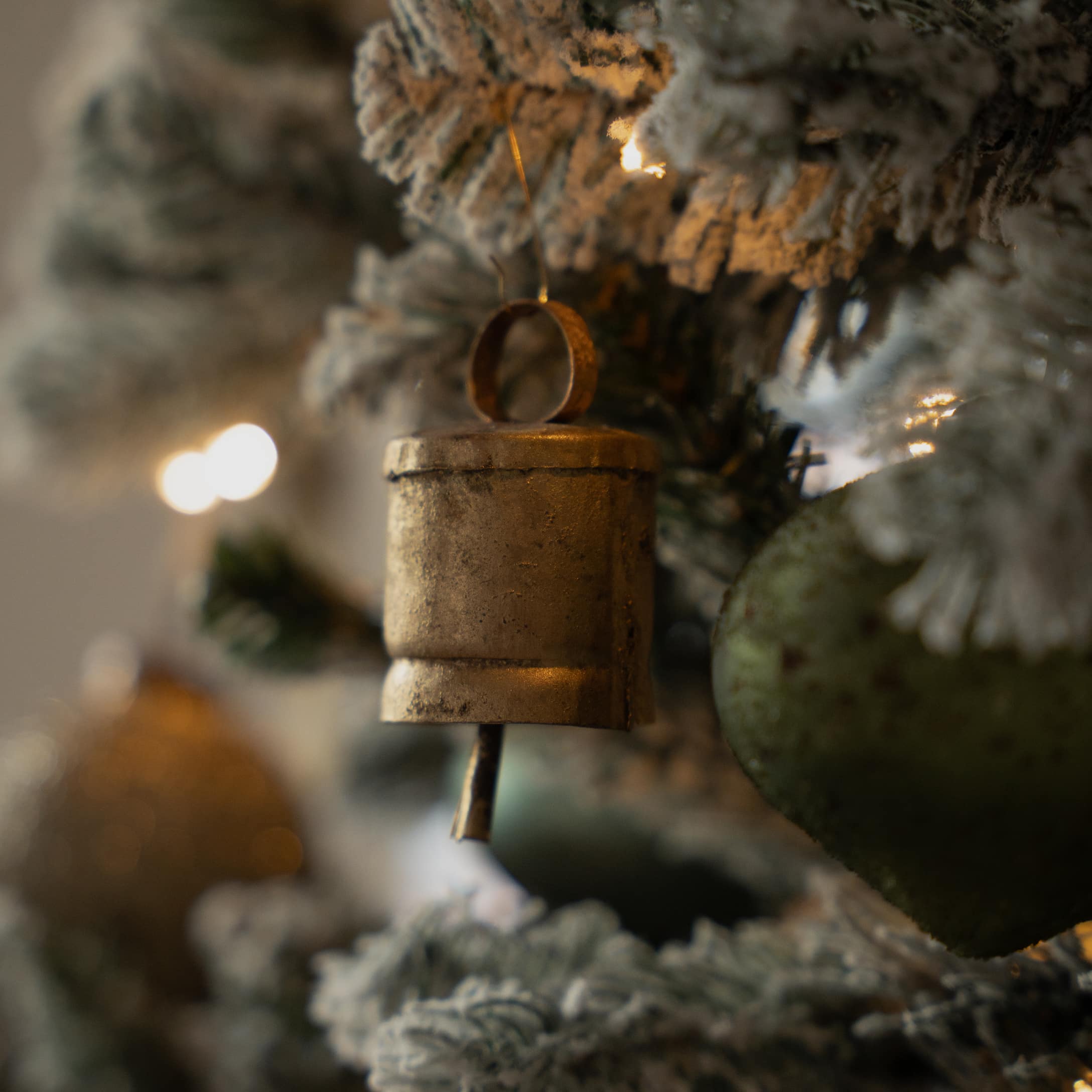 Goldener Metallglöckchen-Anhänger an schneebedecktem Weihnachtsbaum mit Herzdekoration