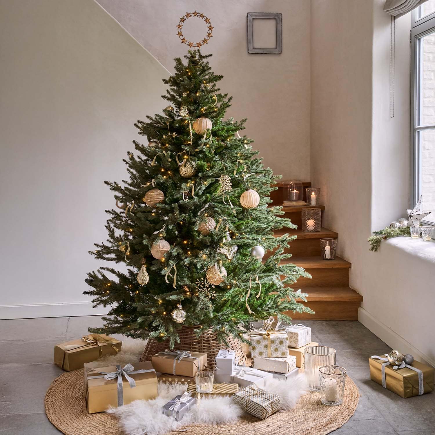 Grüner Weihnachtsbaum mit natürlichen Dekorationen und goldenen Geschenken auf rundem Teppich im hellen Raum