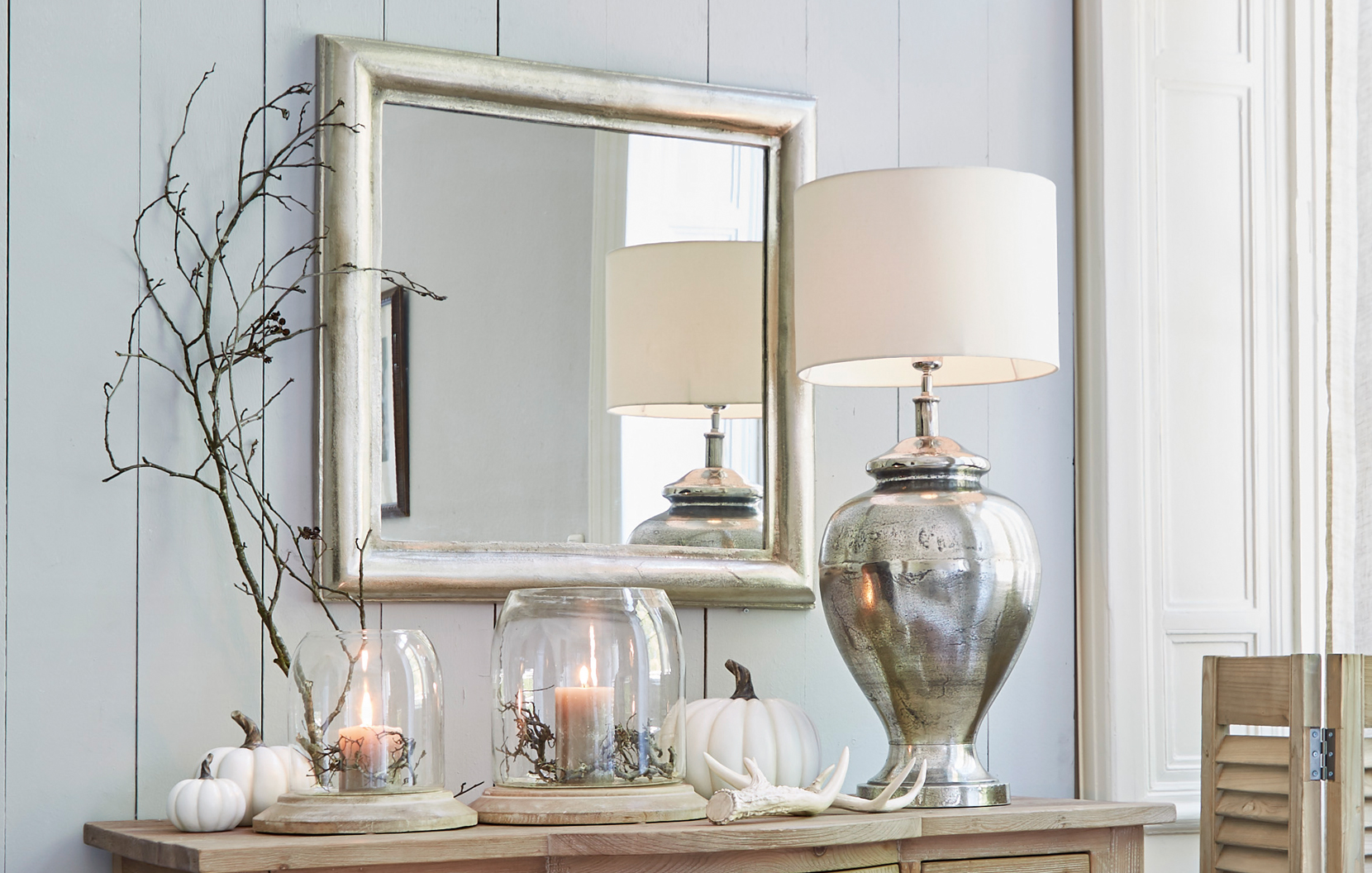Klassisch elegantes Interieur mit silbernem Spiegel, Metalllampe und Dekorationen auf Holzkommode.
