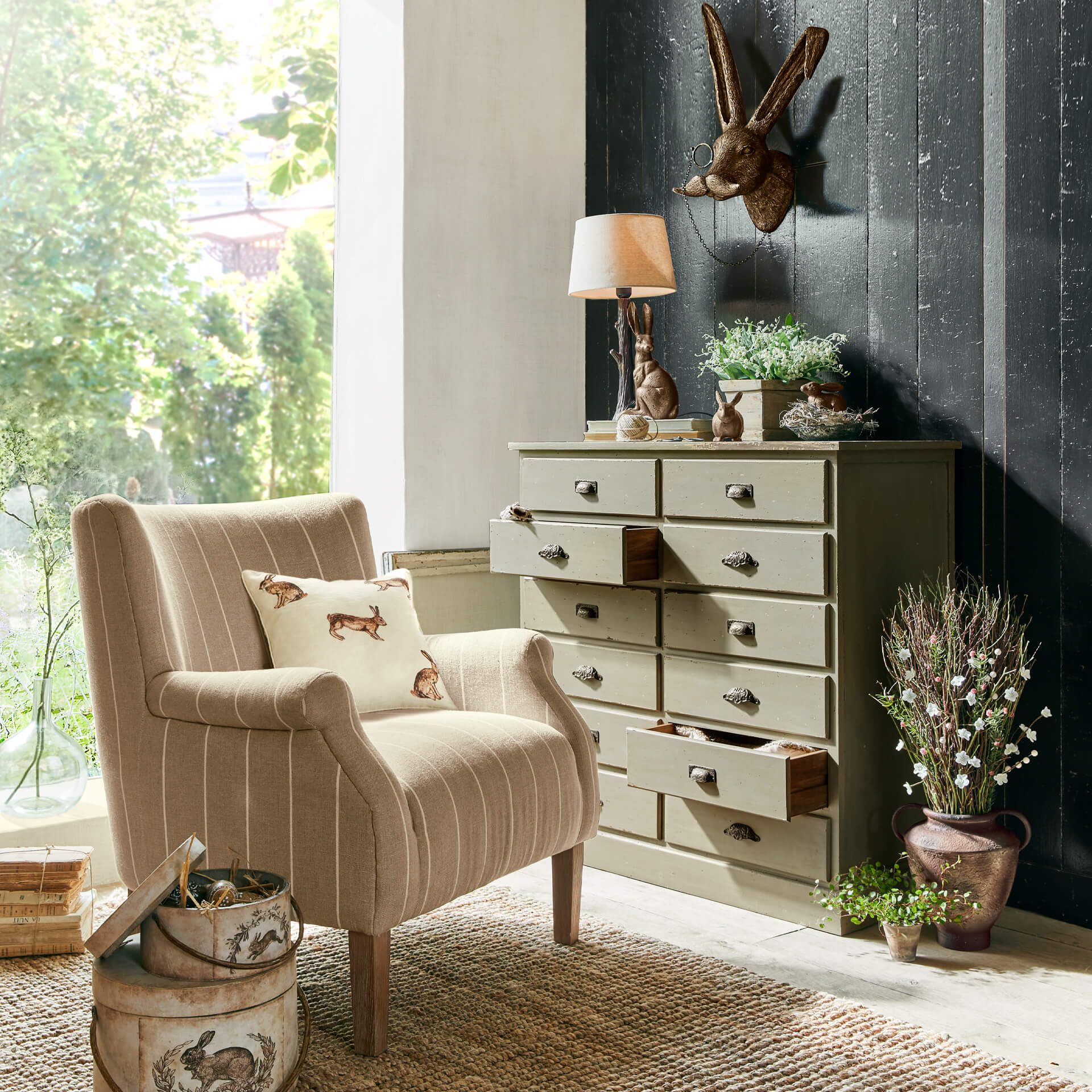 Beiger Stoffsessel mit Hasenkissen neben grüner Kommode und rustikaler Dekoration im Wohnzimmer