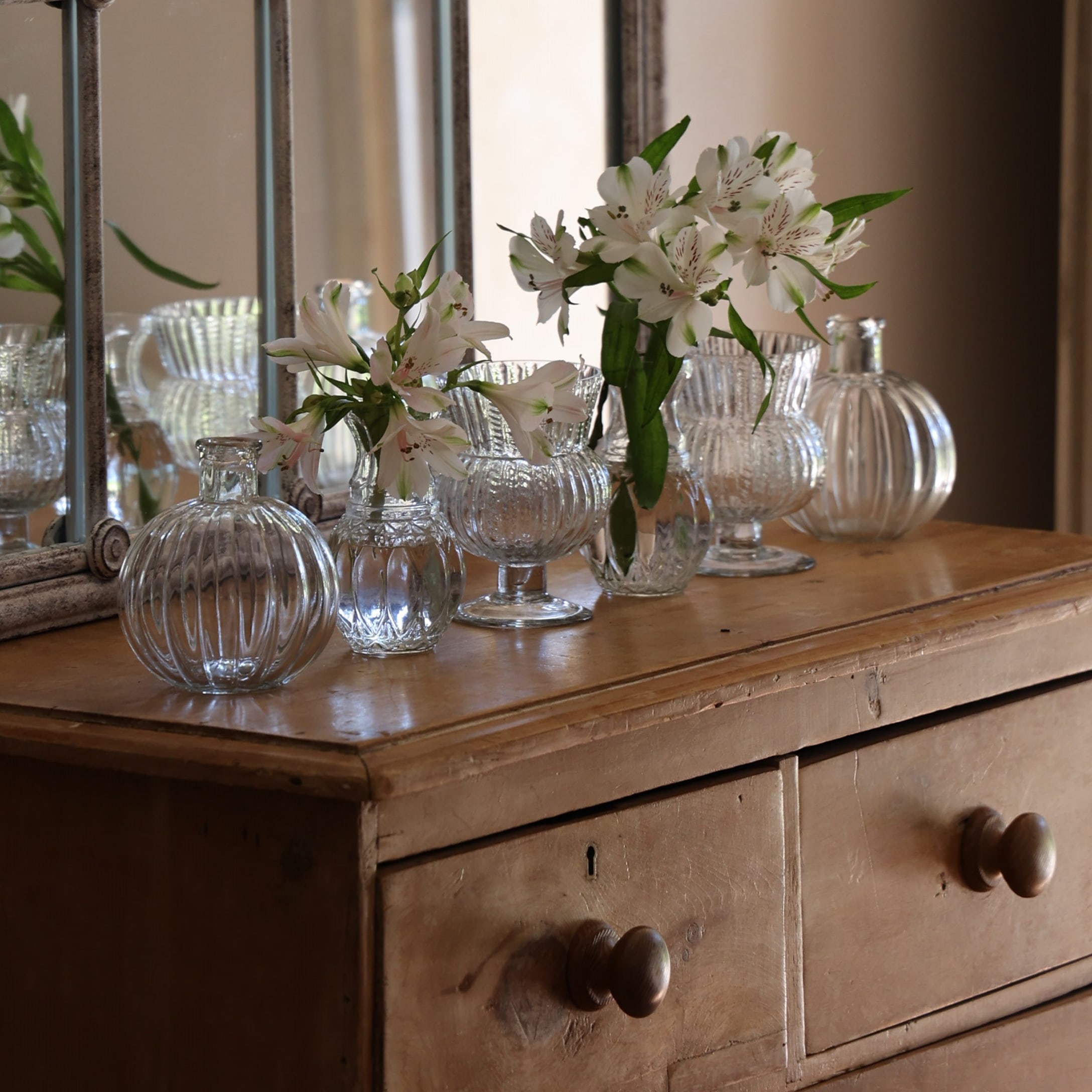 Transparente Glasvasen mit weissen Blumen auf einer Vintage-Holzkommode dekoriert
