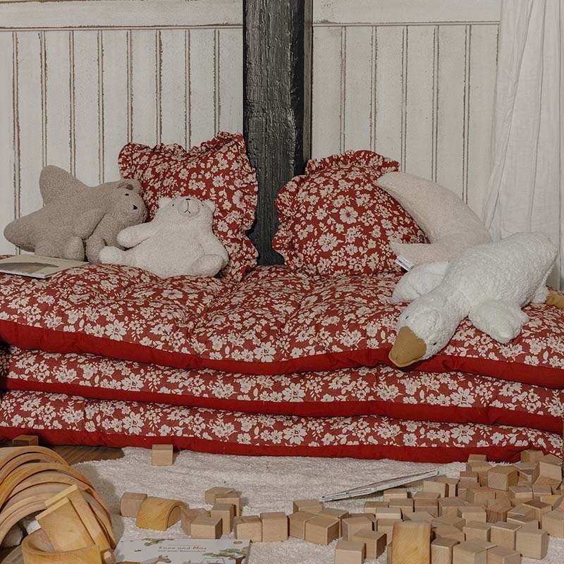 Rote Blumenmuster-Kissen und Matratzen mit Plüschtieren in einer Kinderspielecke mit Holzbausteinen