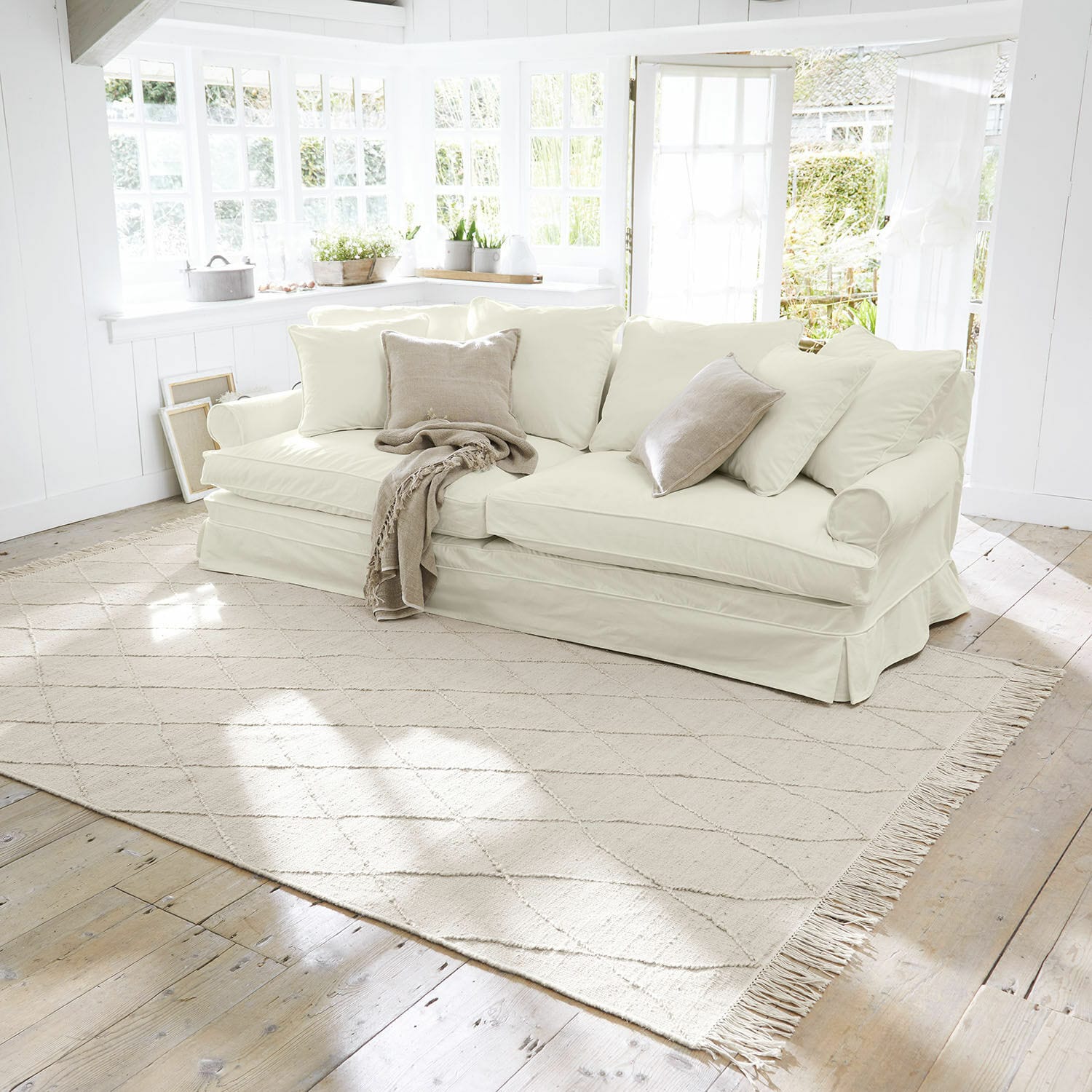 Teppich Ivonique Beiges helles Sofa mit weichen Kissen und Decke in einem hellen, gemütlichen Wohnzimmer