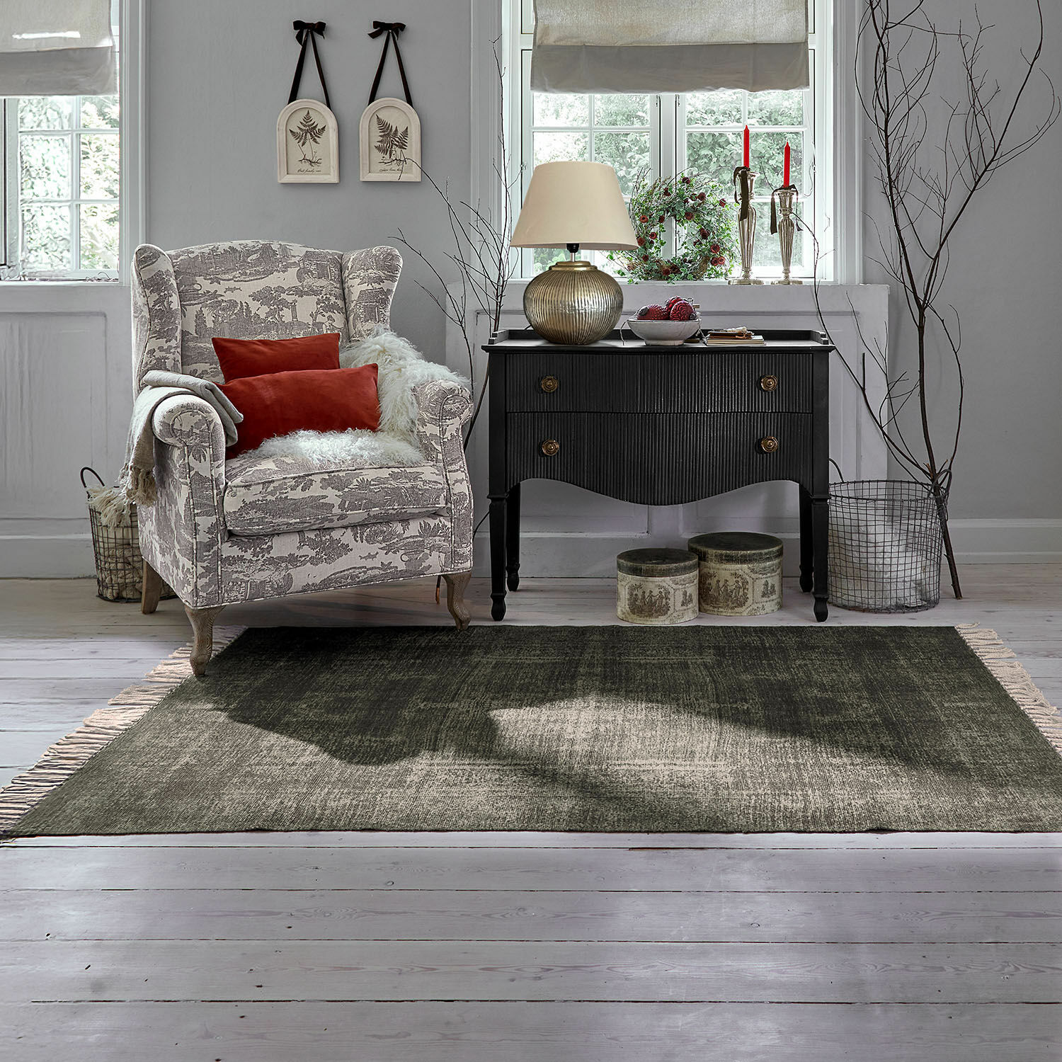 In- & Outdoor-Teppich Belaric Gemütlicher Sessel mit beige-grauem Muster und roten Kissen neben schwarzer Vintage-Kommode im Wohnzimmer