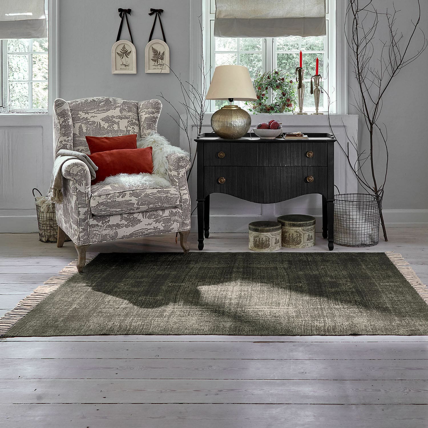 In- & Outdoor-Teppich Belaric Gemütlicher Sessel mit beige-grauem Muster und roten Kissen neben schwarzer Vintage-Kommode im Wohnzimmer