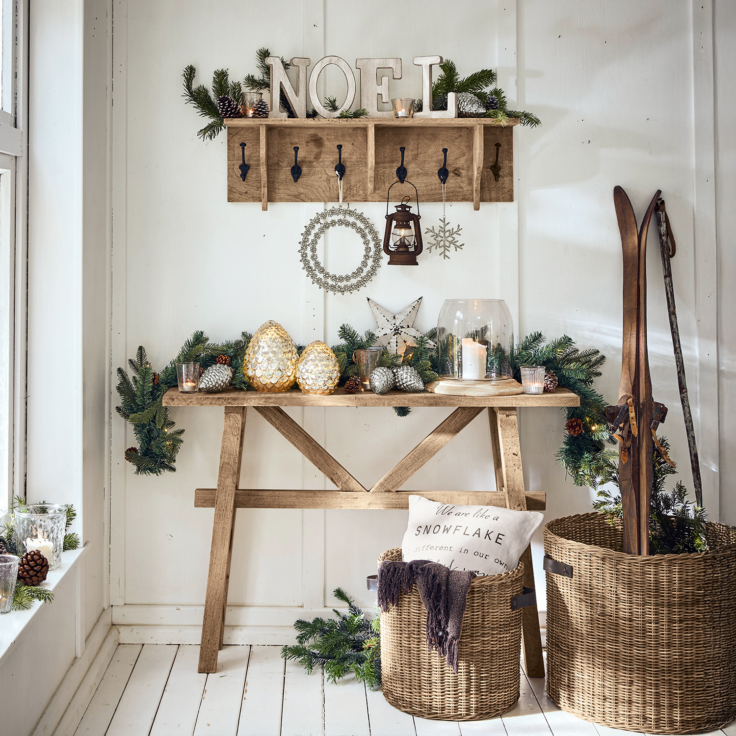 Holztisch und Garderobe mit Weihnachtsdekoration, Laterne und Weidenkorb mit Skiern