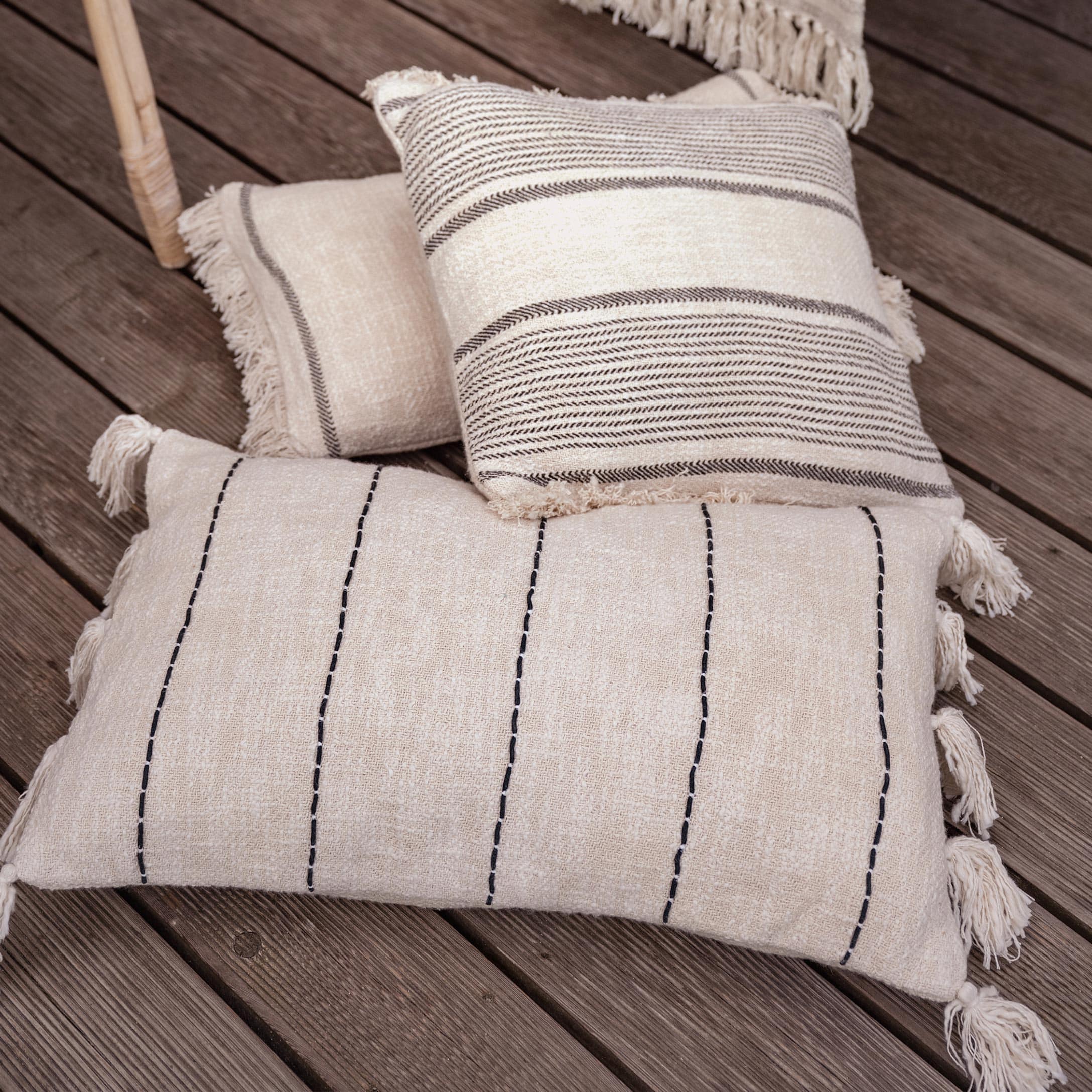 Beiges Baumwoll-Dekokissen mit Fransen und Mustern auf Holzboden, Wohnaccessoire im Boho-Stil