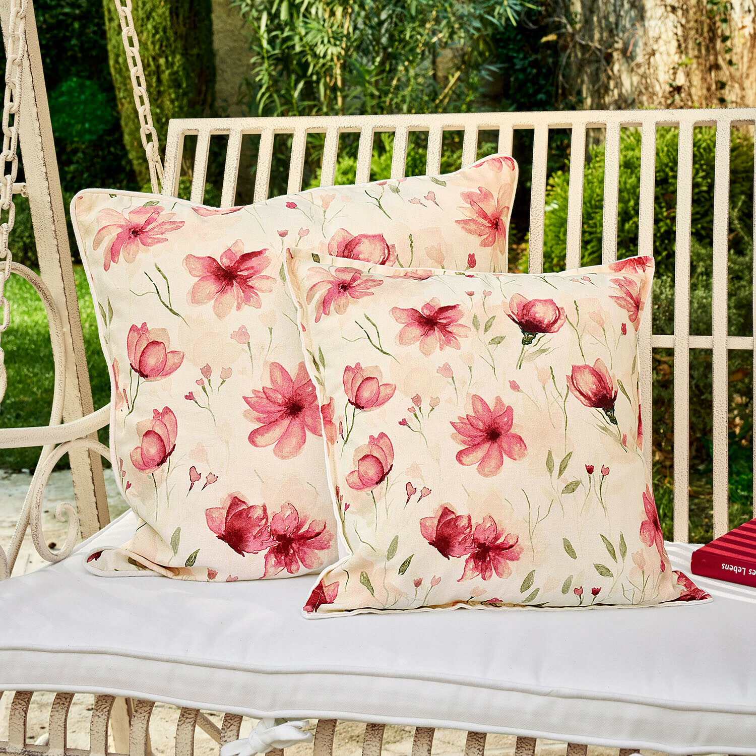 Zwei dekorative Kissen mit Blumenmuster auf weisser Gartenschaukel, Baumwollstoff, hellrosa Blumen
