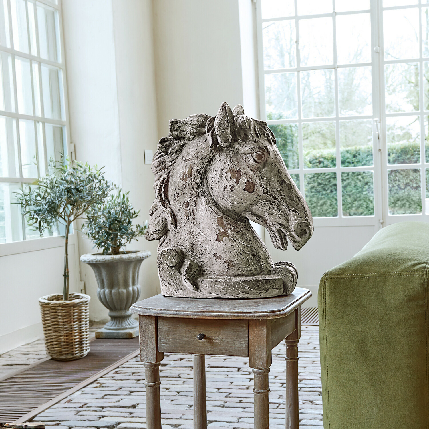 Deko-Pferd Ghenire Skulptur eines Pferdekopfes aus antik anmutendem Stein auf Holzbeistelltisch neben grünem Sofa mit Kissen