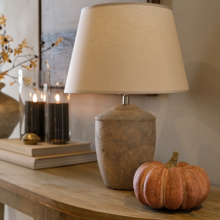 Tischlampe mit beigem Schirm und steinerner Basis auf Holztisch mit Kürbisdekoration
