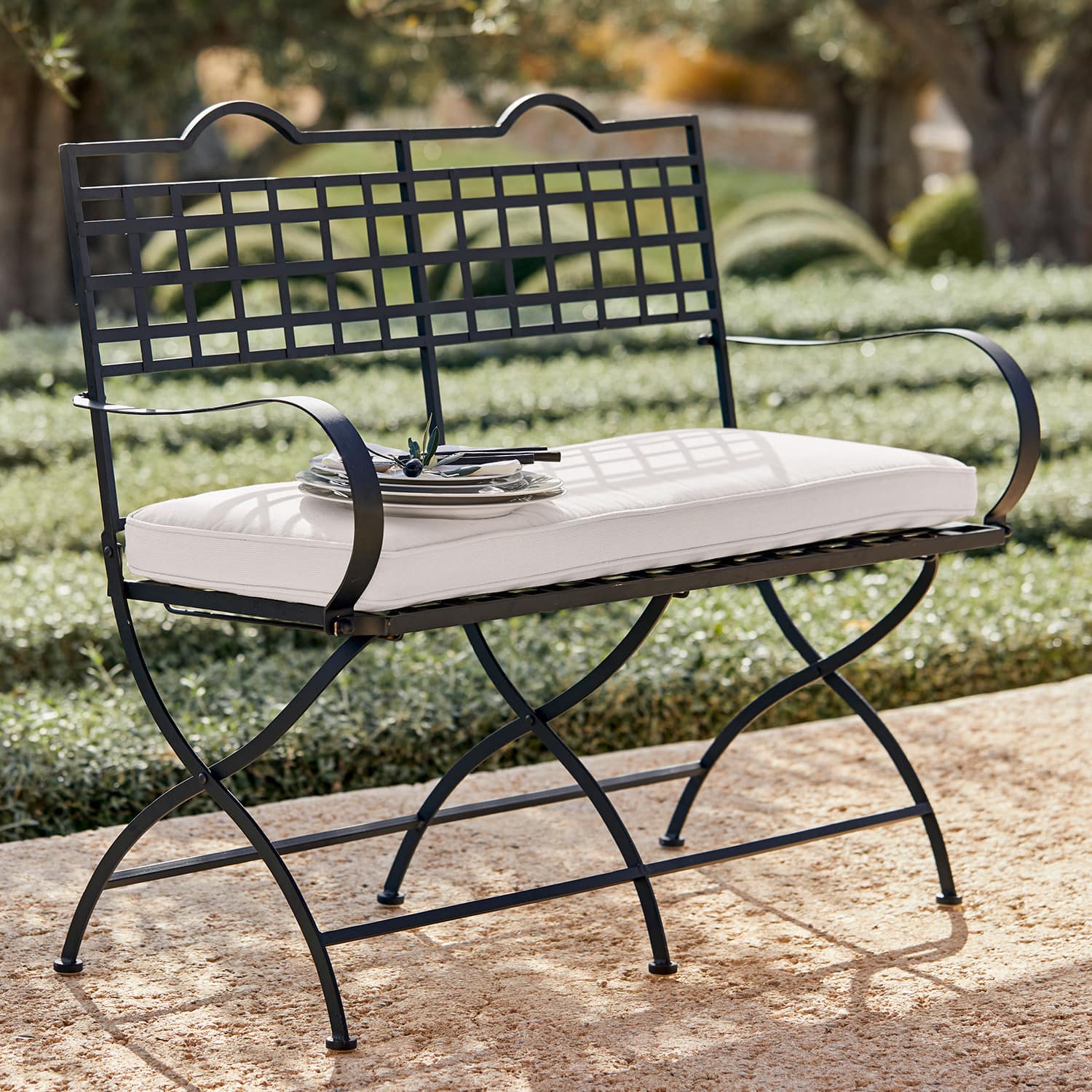 Schwarze Metall-Gartenbank mit weissem Sitzkissen auf steinerner Terrasse im Freien