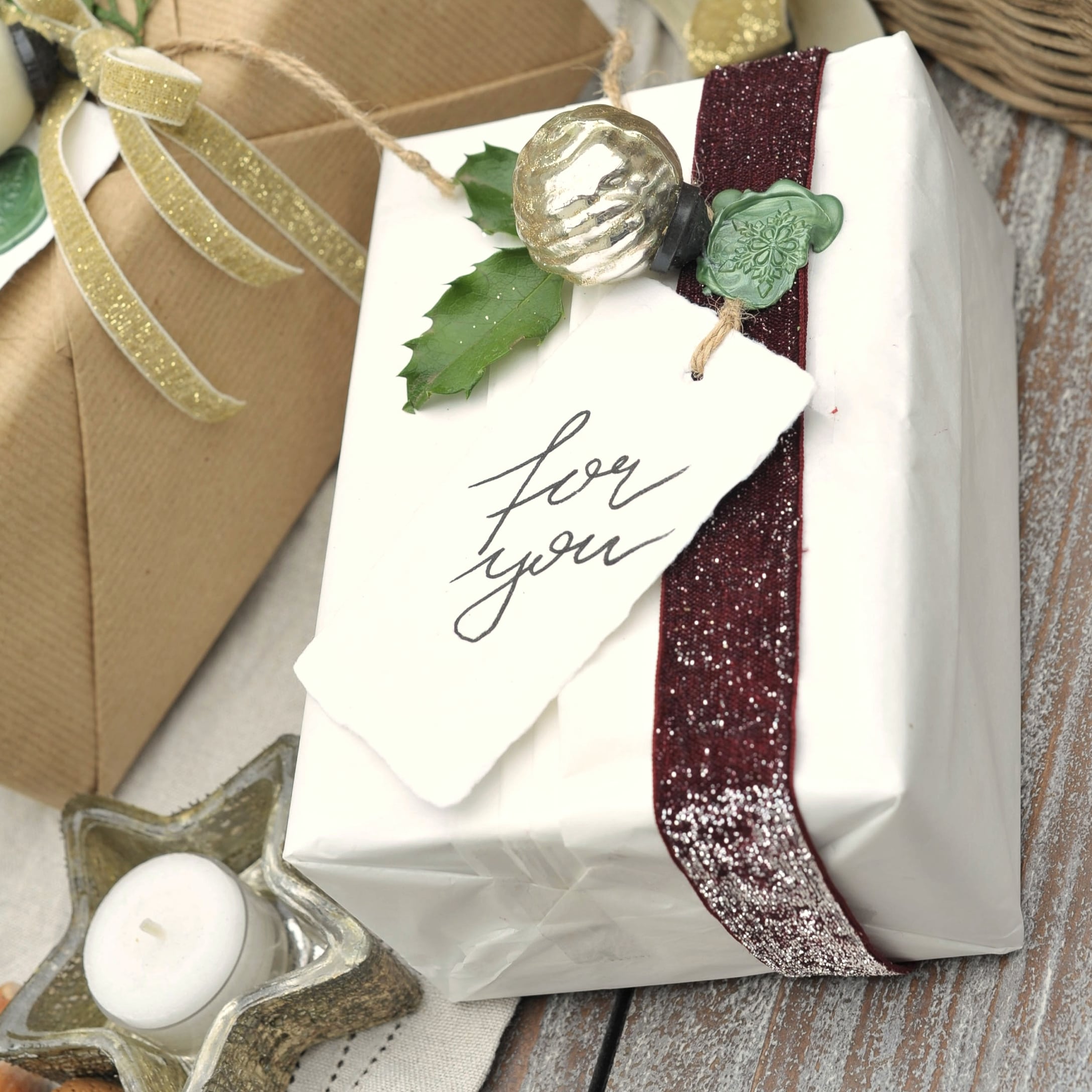 Weiss verpacktes Geschenk mit bordeauxrotem Band und grünem Stechpalmenblatt als Dekoration