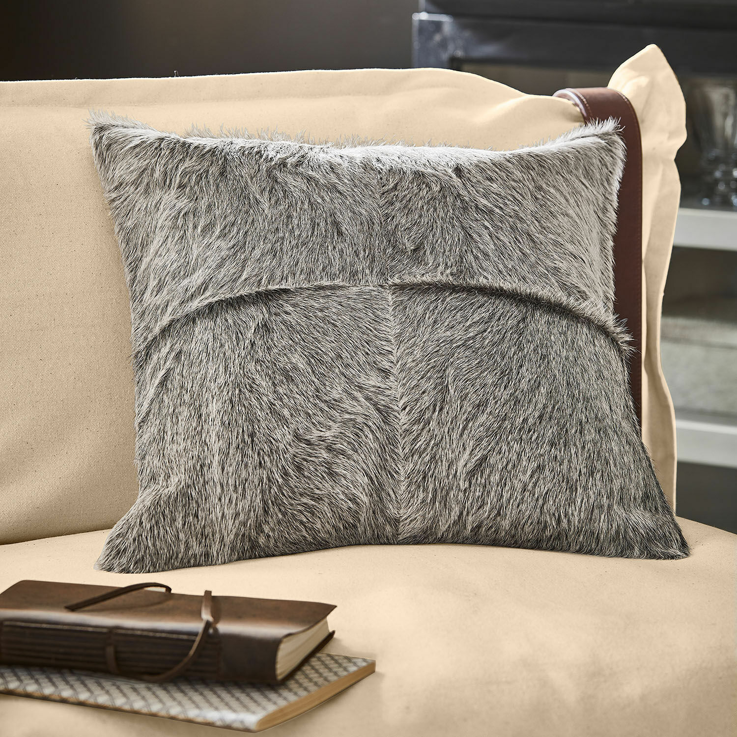 Kissenhülle Nymarion Graues Dekokissen aus Fellmaterial auf beigem Sofa, stilvolles Wohnaccessoire für Gemütlichkeit.
