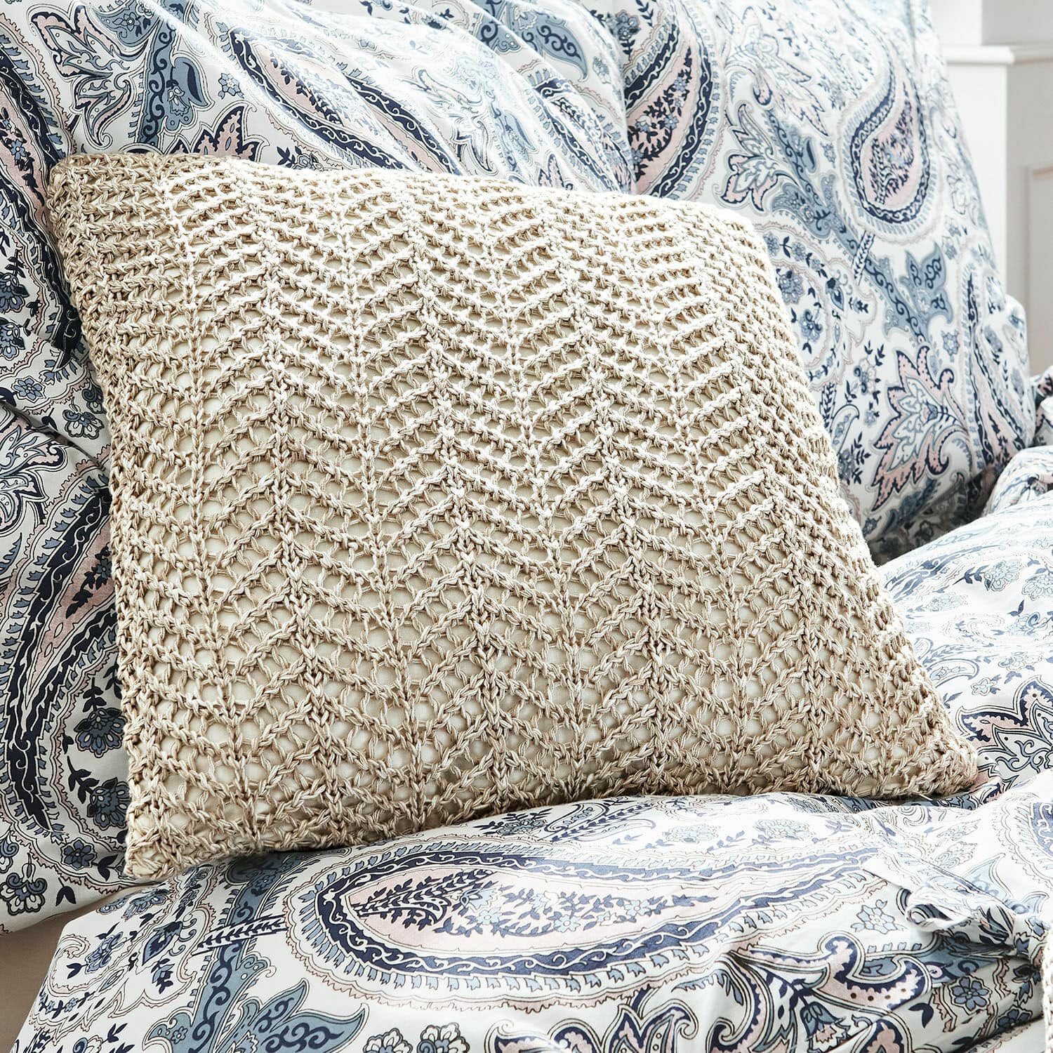 Beiges Kissen mit geflochtenem Muster auf blau-weiss gemustertem Paisley-Bezug