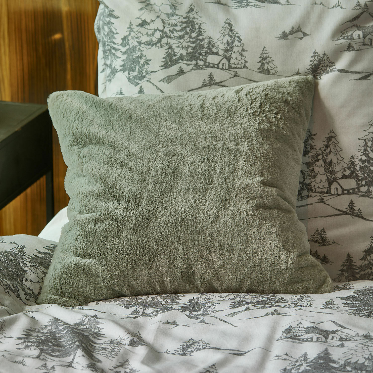 Kissenhülle Léorienne Weiches grünes Plüschkissen auf Bett mit grauem Baum- und Hausmuster-Bettbezug
