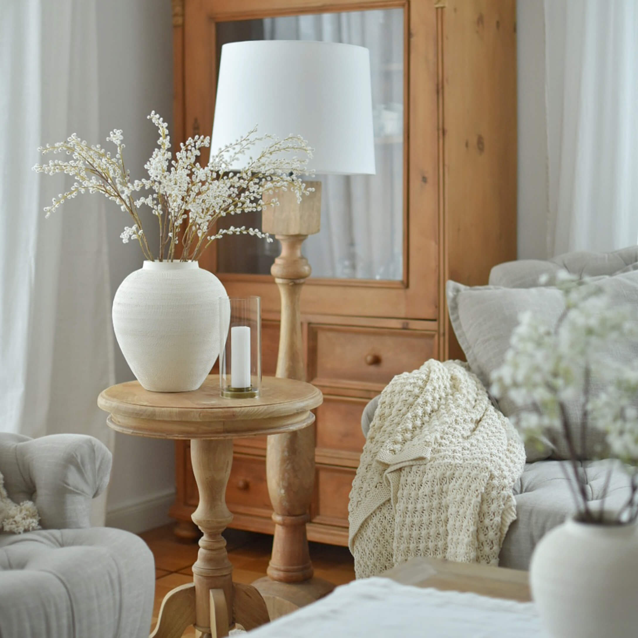 Heller Holztisch mit weisser Keramikvase und Lampe in gemütlichem Wohnzimmer mit beiger Decke