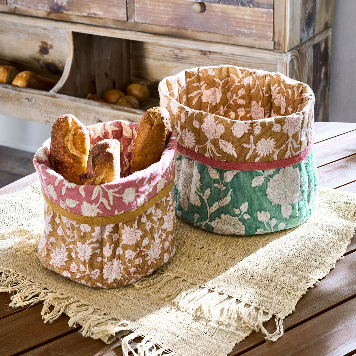 Zwei dekorative Baumwollkörbe mit Blumenmuster in Rosa, Braun und Grün für Brot auf Holztisch