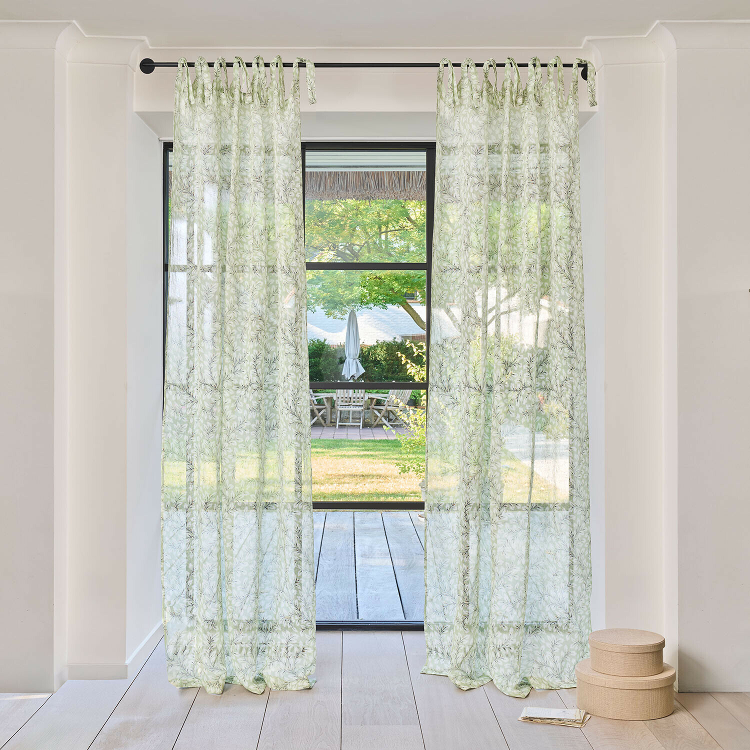 Gardine Norelline Transparente Vorhänge mit grünem Blattmuster an schwarzer Stange in hellem Raum mit Gartenblick